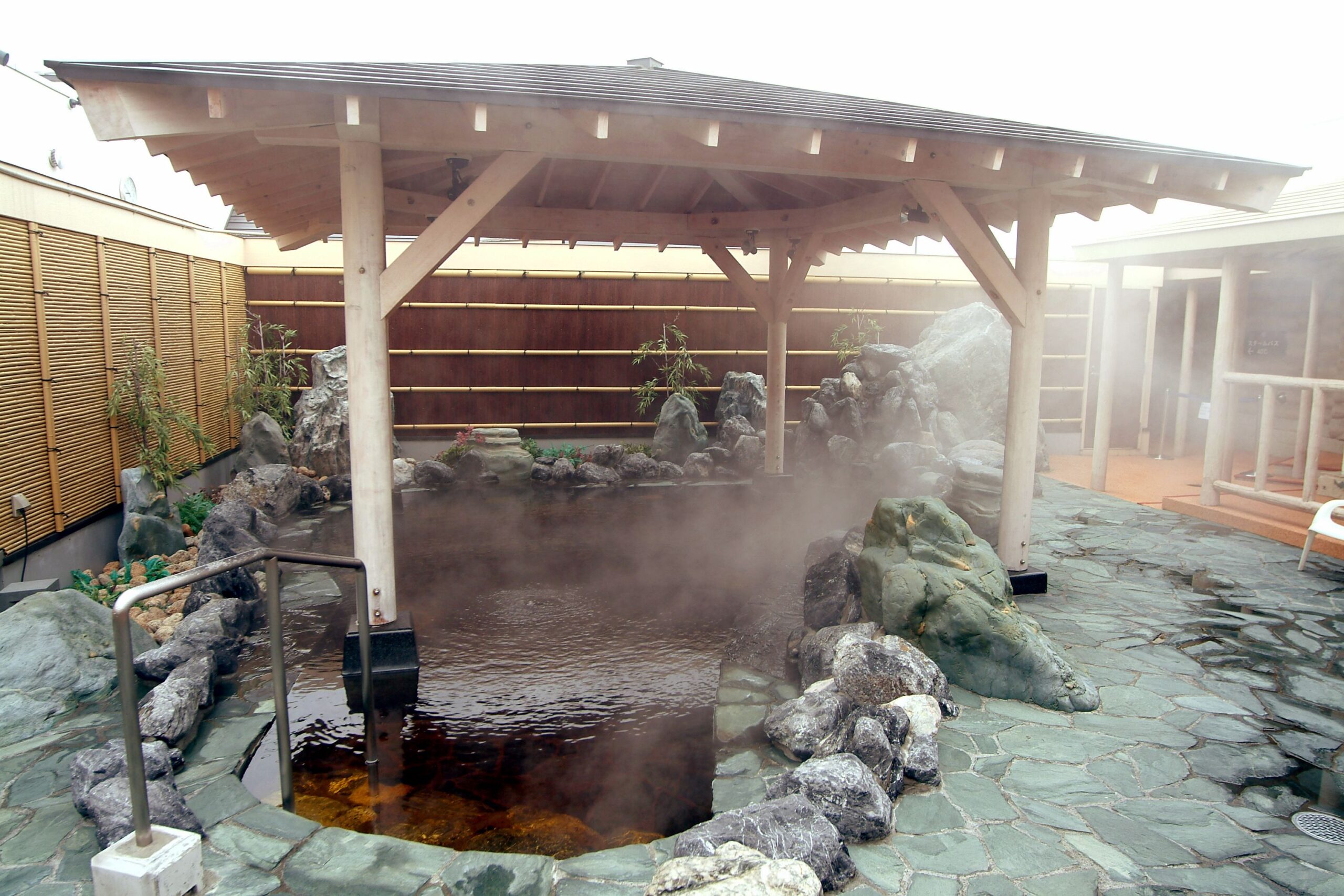 An outdoor onsen in Chateraise Gateaux Kingdom Resort and Spa, a large resort hotel in Sapporo, Japan. There is steam rising from the onsen bath, and the floor has stone decor. There is a small pagoda over the open air bath.