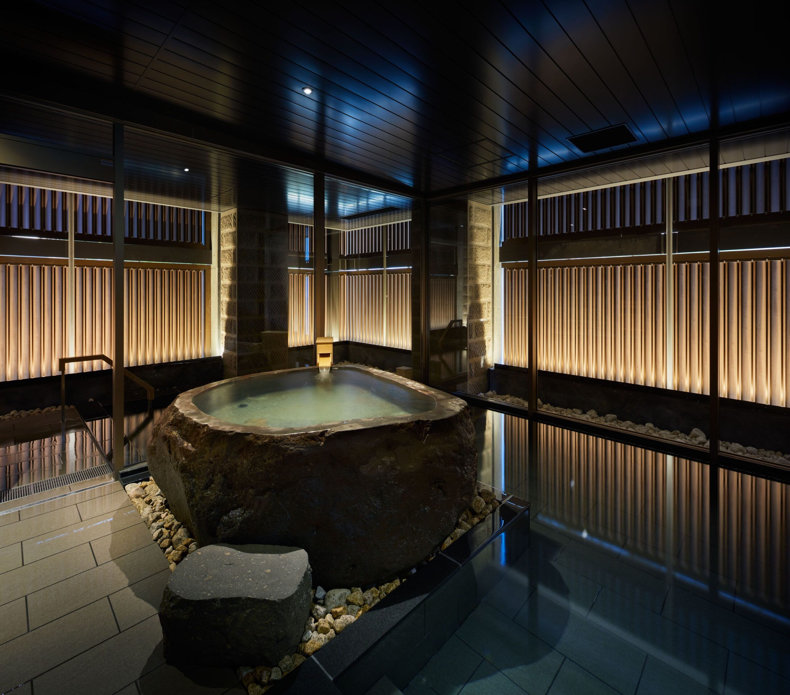 A Japanese style public onsen, with a stone bath hot tub and a large pool of water around it. From Onsen Ryokan Yuen in Sapporo, Japan.