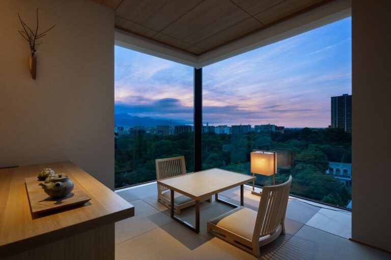 A hotel room in Ryokan Onsen Yuen, a popular ryokan in Sapporo, Japan. In the room there is a table with japanese style chairs, and a beautiful view of Sapporo skyscrapers and trees.