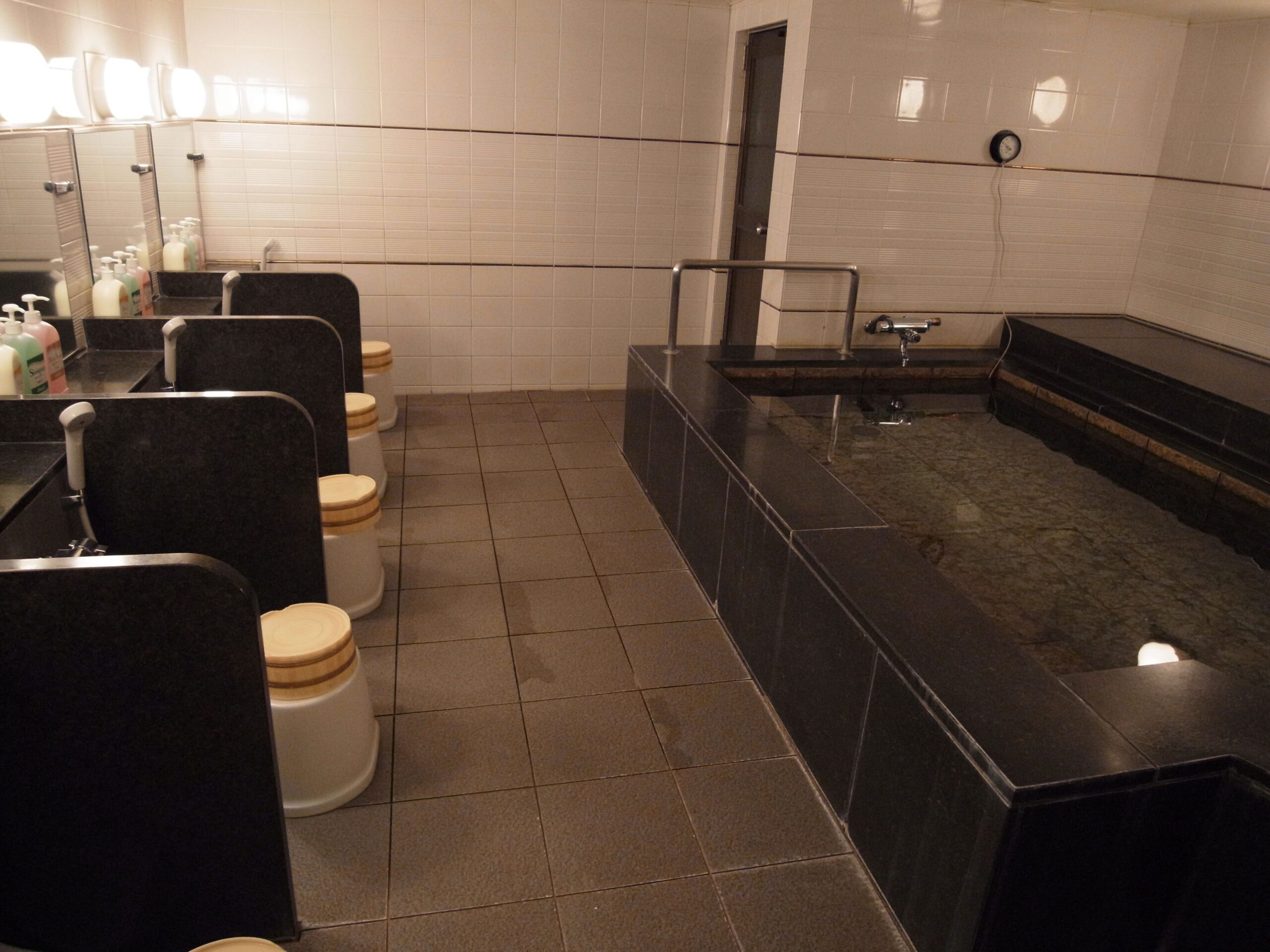A public onsen, with a black onsen tub on the right side. On the left side there are showers. This onsen is available at Nakamuraya Ryokan Sapporo, Japan.