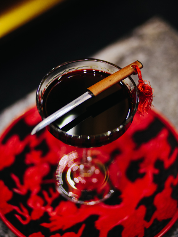 A cocktail with dark liquor and a decorative knife placed on top. Unique drinks are common in Golden Gai, a drinking area in Tokyo, Japan