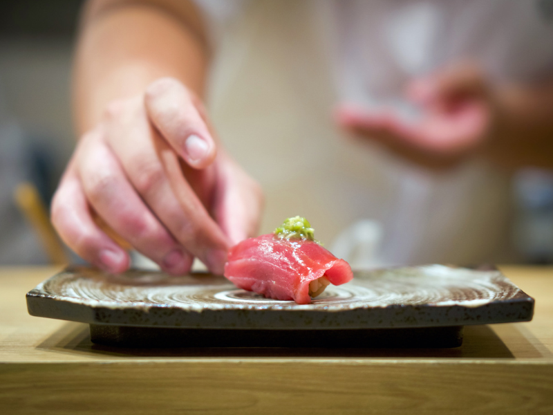 Close-up of a single piece of omakase tuna sushi, with a vibrant red slice of tuna resting on a small mound of seasoned rice.