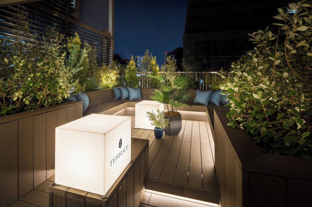 The rooftop terrance of Tokyu Stay Shibuya. There are large glowing cubes, luscious greenery and a beautiful rooftop view.