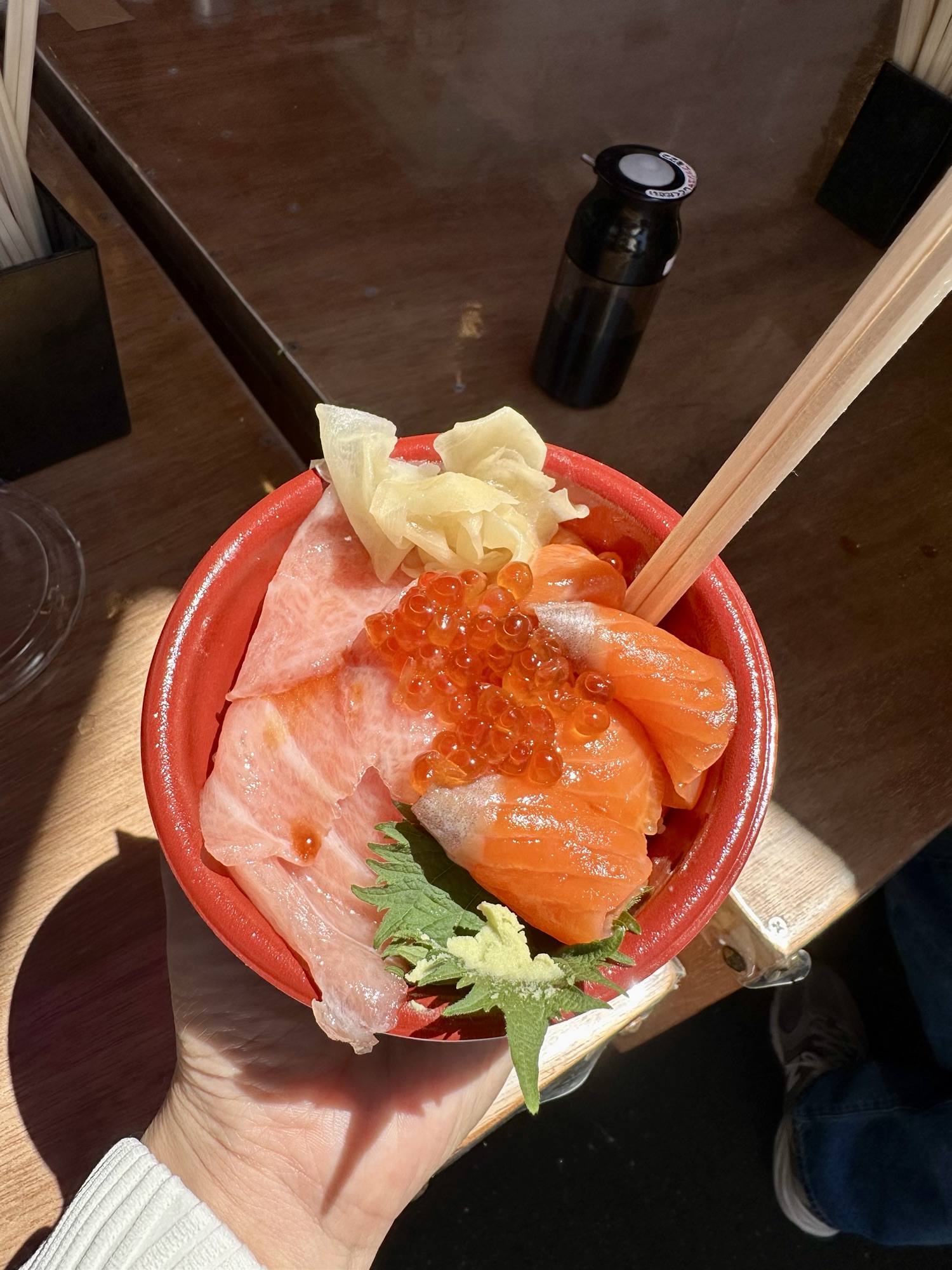 A vibrant seafood donburi from Tsukiji Market, featuring fresh slices of salmon and toro belly arranged over rice, garnished with pickled ginger and a dollop of wasabi.