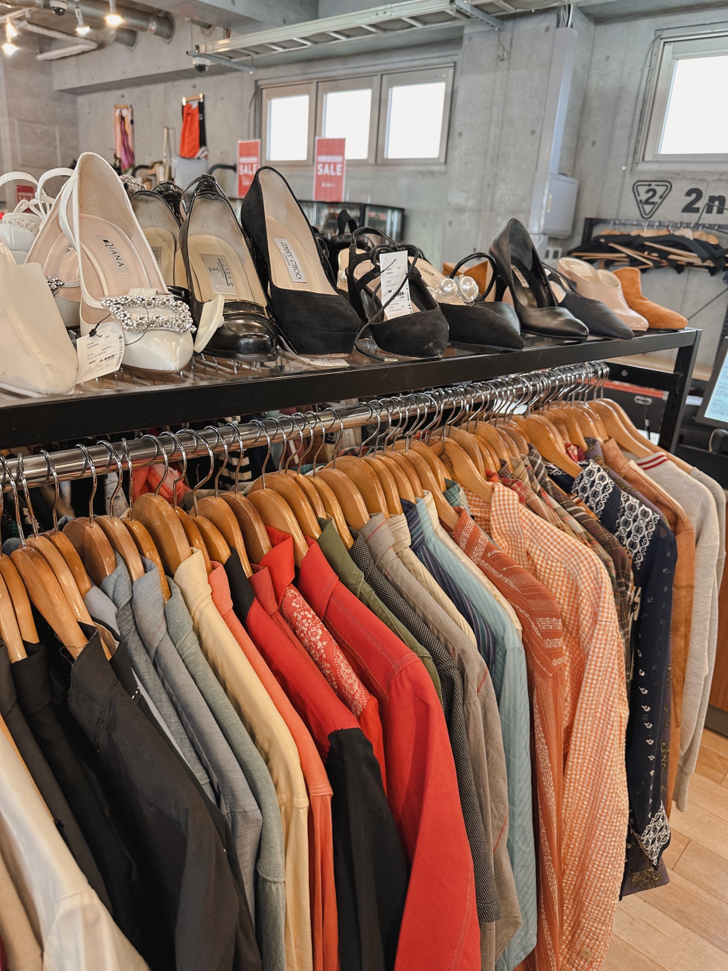 Lots of thrift clothing stores are in Harajuku. There are pairs of shoes on top of a clothing rack with lots of colorful options.