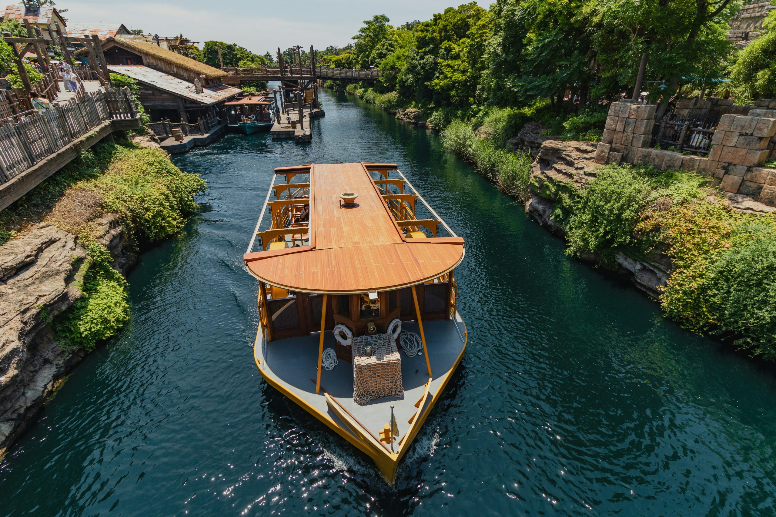 A boat sailing on teal-colored water at Tokyo DisneySea, with vibrant attractions and a clear sky in the background.