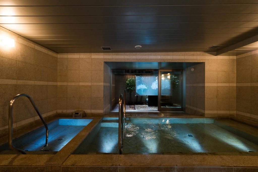 The public onsen of Super Hotel Premier Tokyo Station Yaesu Chuo. There are two large baths with hot spring water, illuminated with warm lights encouraging a relaxing atmosphere.