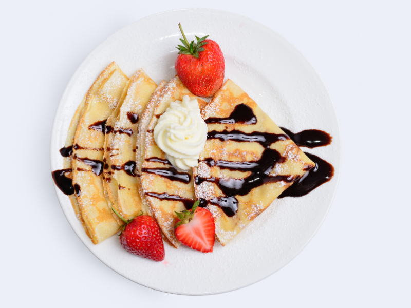 A crepe with whipped cream, strawberries, and chocolate drizzle on top. 