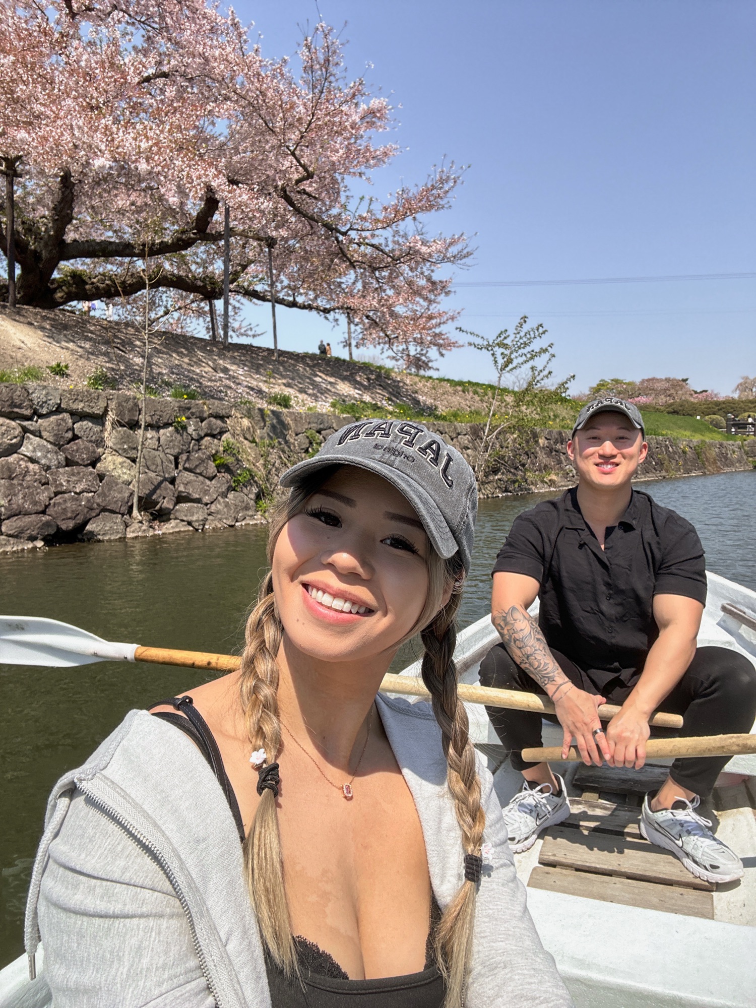 A woman and man in a boat in Goryokaku Fort. There are blossoming cherry trees in the back.