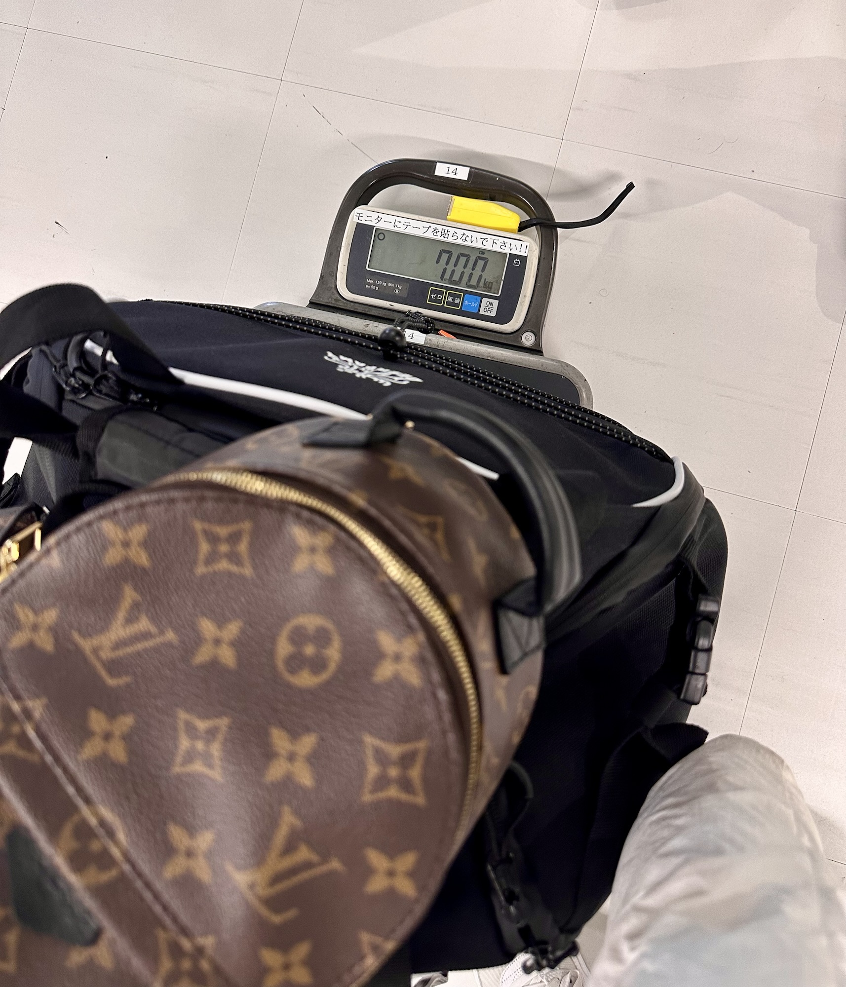 A luggage scale showing 7.0 kg, with a black bag and Louis Vuitton backpack on the scale in Hakodate, Hokkaido Japan.