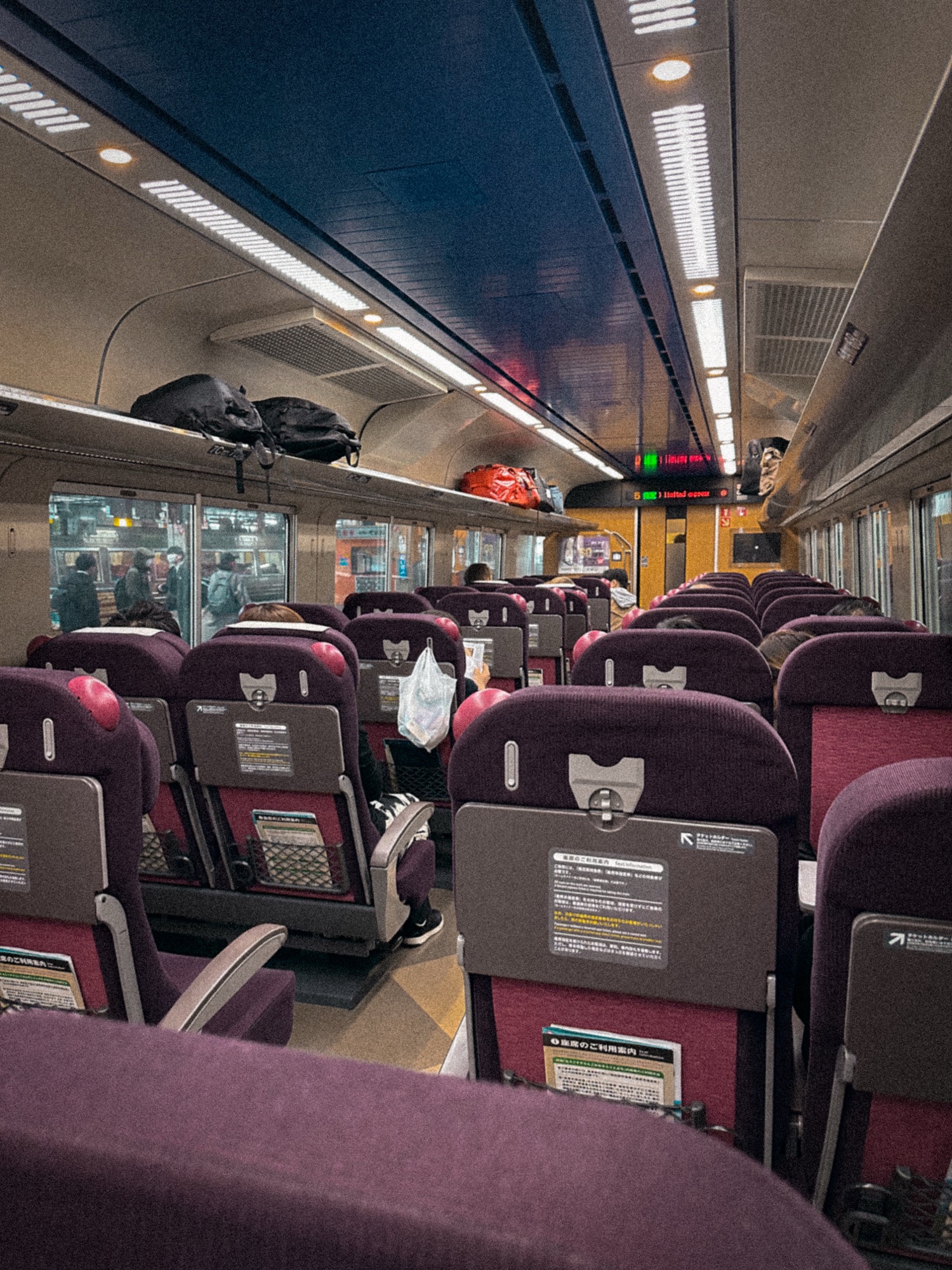 The inside of the Hokuto limited express train connecting Hakodate to Sapporo. The comfortable seats are maroon, with hangers for coats and bags. There is overhead luggage space.