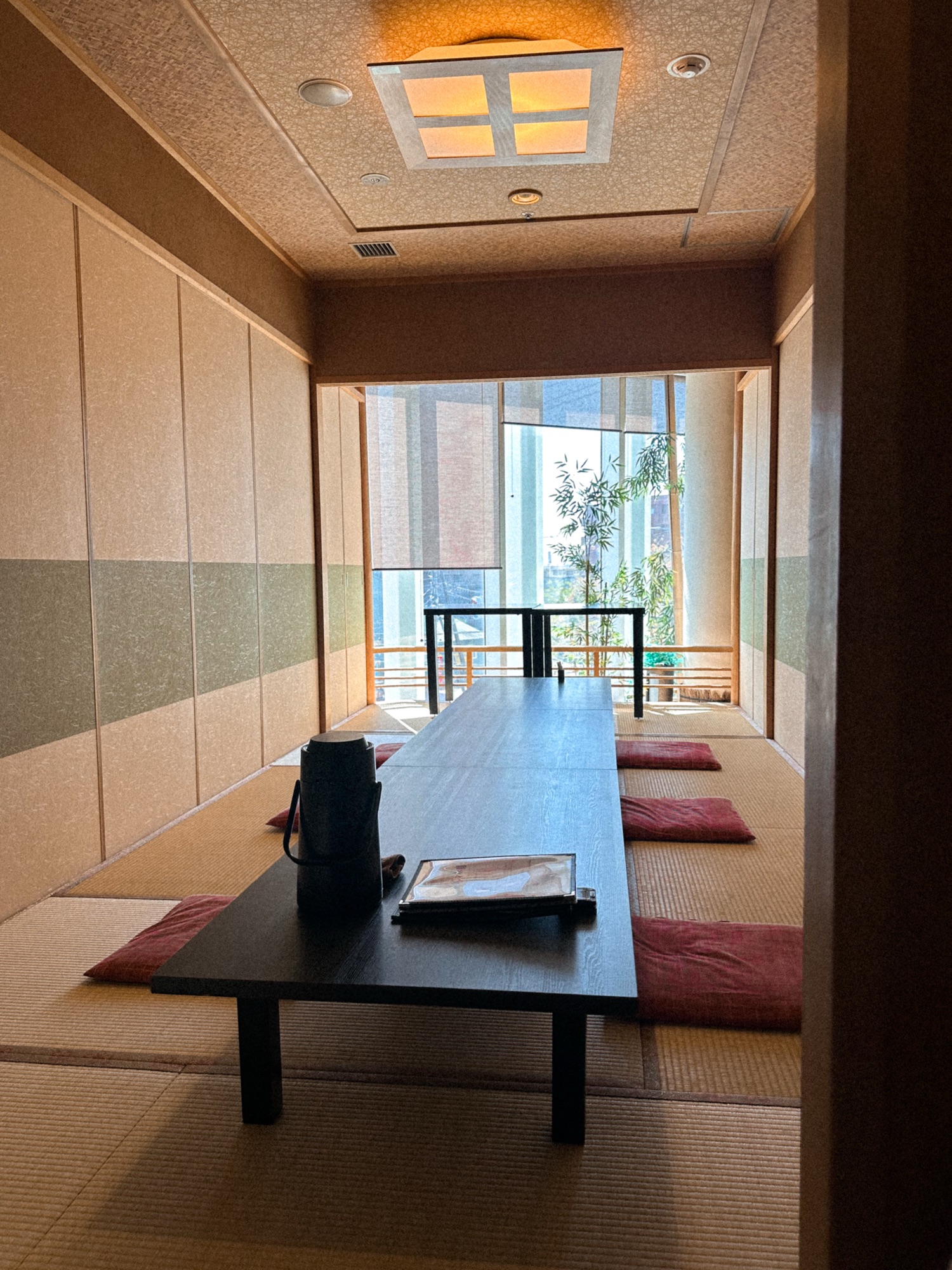 A private tatami room in Seasonal Seafood Shunka, a restaurant in Goryokaku Tower in Hakodate, Hokkaido. There is a long black table with red pillows for sitting. In the back there are floor to ceiling glass windows providing a view of Hakodate.