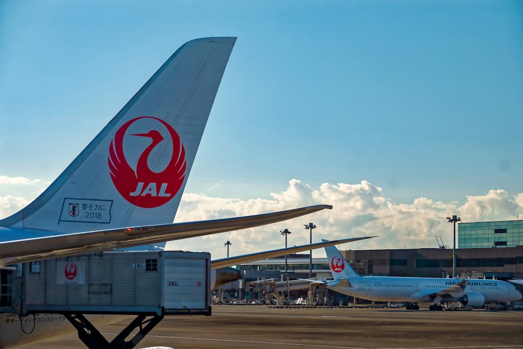 Japan Airlines planes on tarmac at airport under clear blue sky.