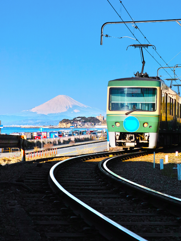 The view of Mount Fuji from Kamakura and Enoshima on a sunny clear day. There is a bright teal public bus on the highway with the mountain in the back.