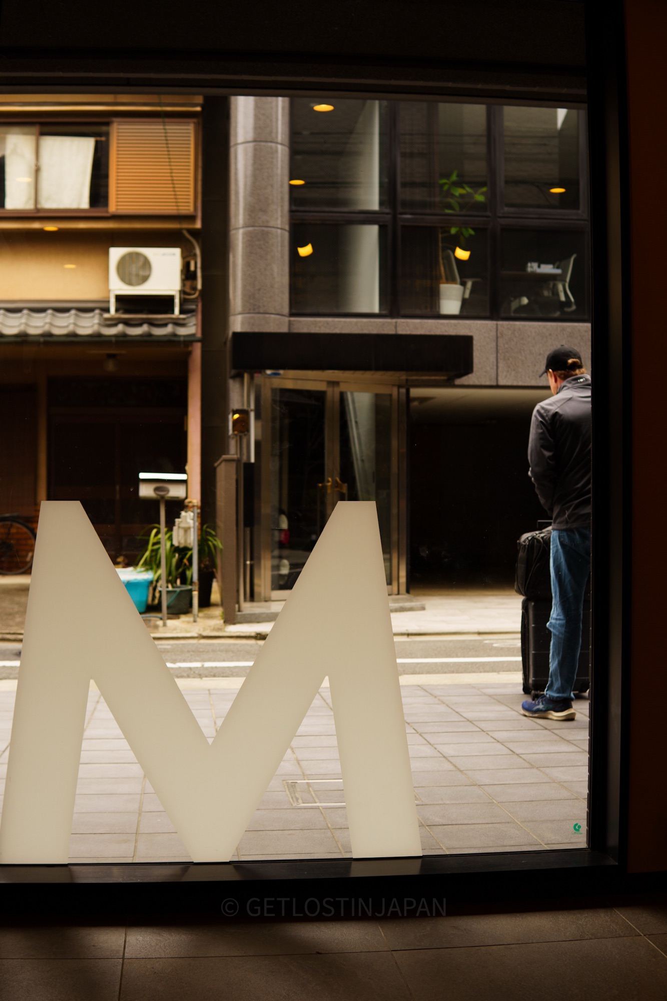 A clear door with a large white "M" printed on it, representing M's Hotel in Kyoto, Japan.