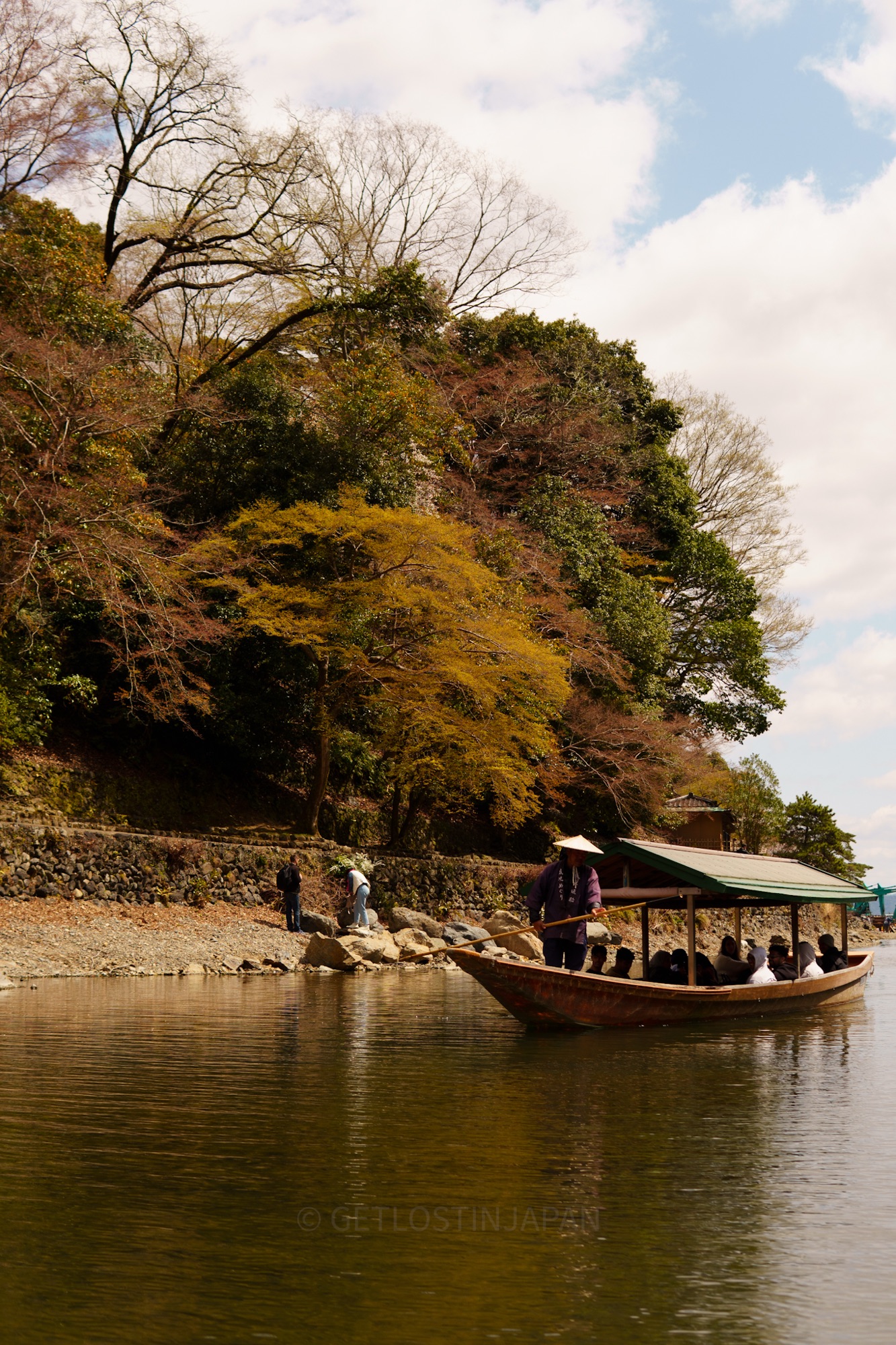 Visitors can enjoy the Hozugawa Boat Ride, a scenic 2 hour boat ride that displays Kyoto's natural beauty. There are large trees with colorful foliage, and a boat passes on the river with people inside.