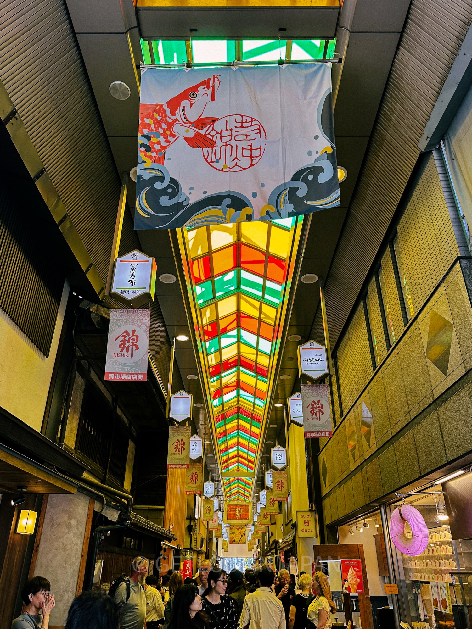Rainbow stained glass in red, yellow, and green cover the ceiling of Nishiki Market in Kyoto, Japan.