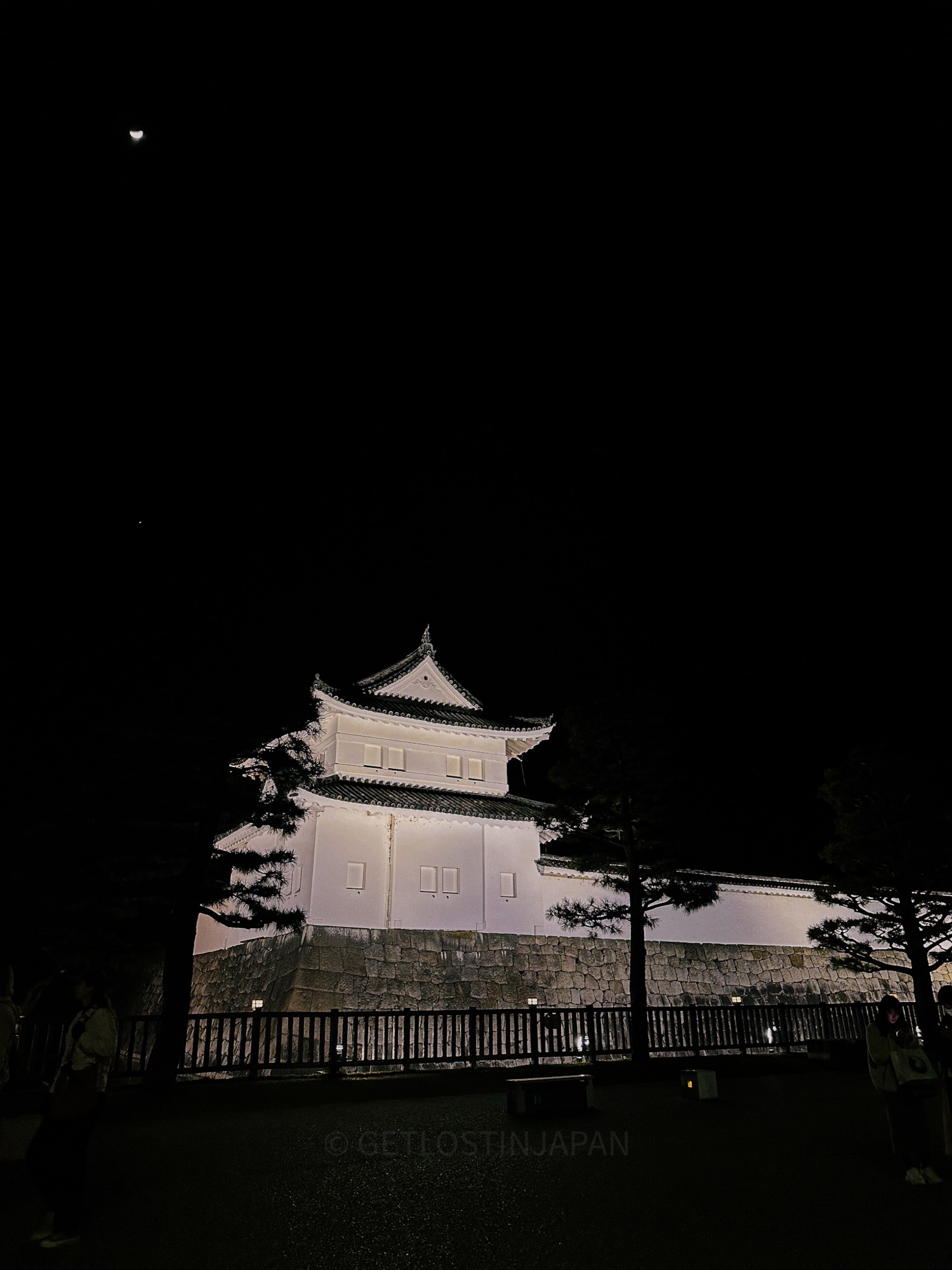 Nijo Castle in Kyoto, Japan at night. The bright white walls of the castle stand out beautifully in the dark night.