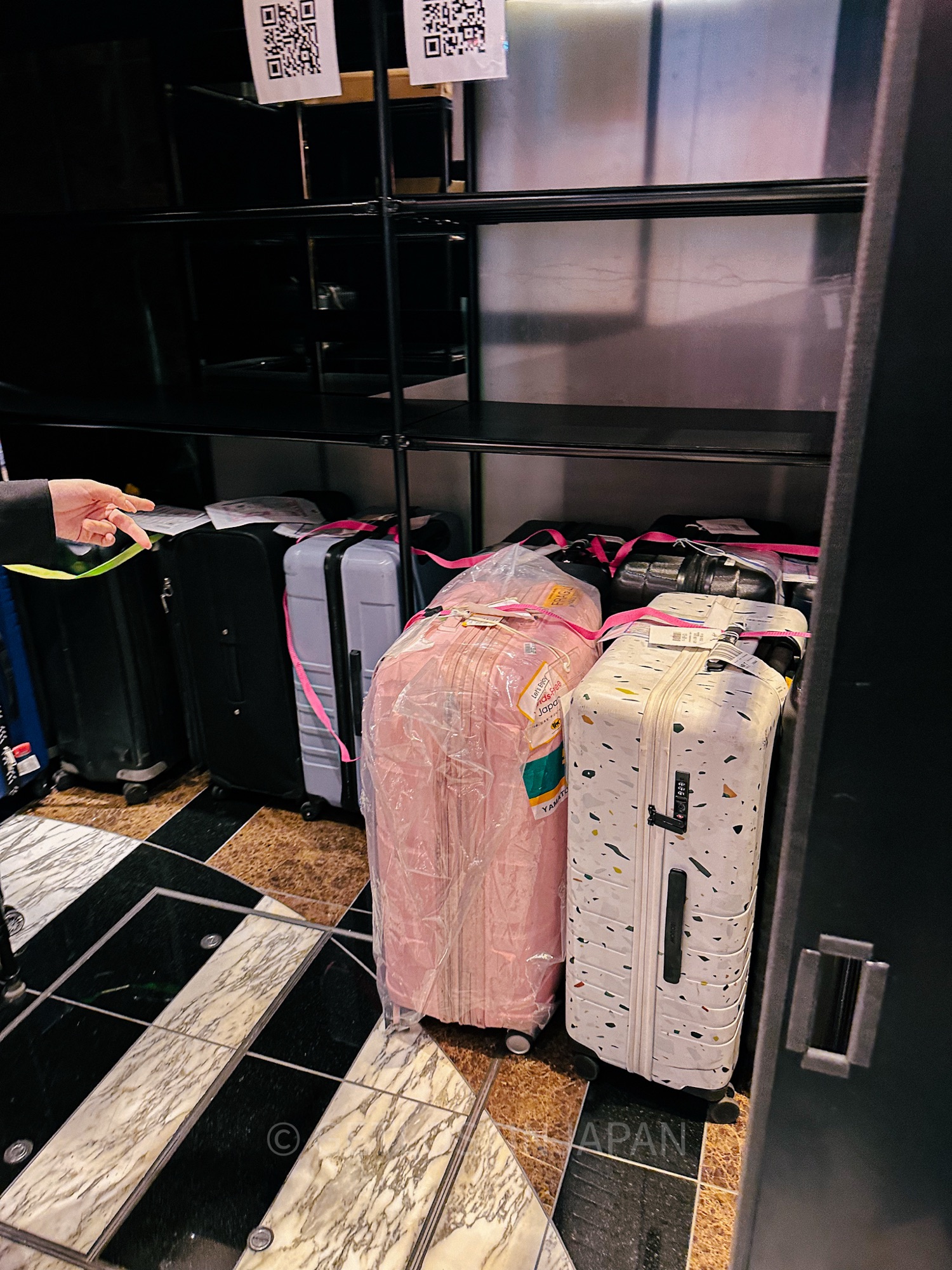 Two full sized luggage in pink and white are being stored after being shipped through Japan's luggage delivery service.