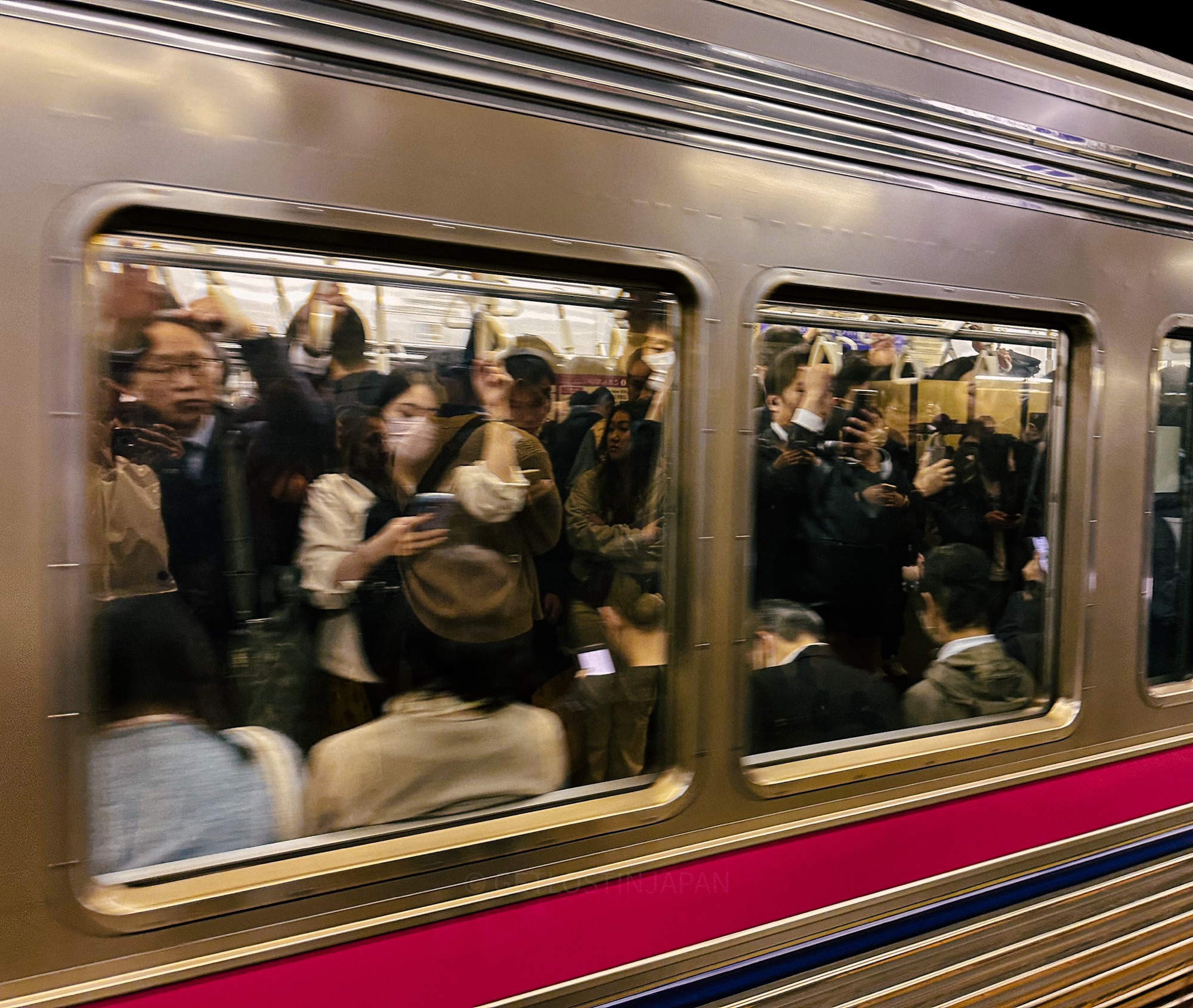 A passing train in Japan. Two train windows show that the vehicle is filled with people.