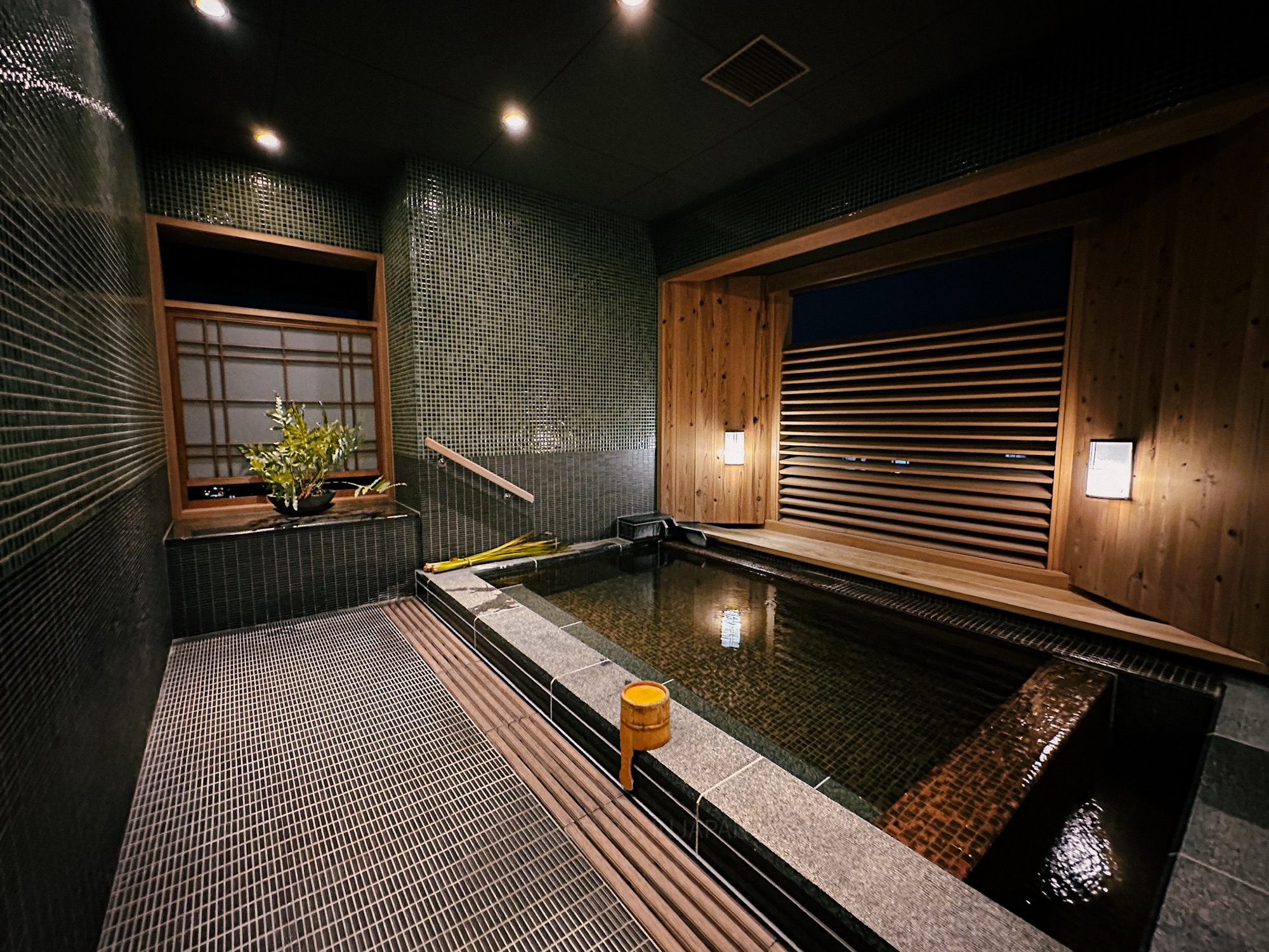 A private onsen in Saka Hotel Kyoto. The ceramic stone onsen features a large window with wooden screen blinds, with wood accents promoting a calm, relaxing environment.