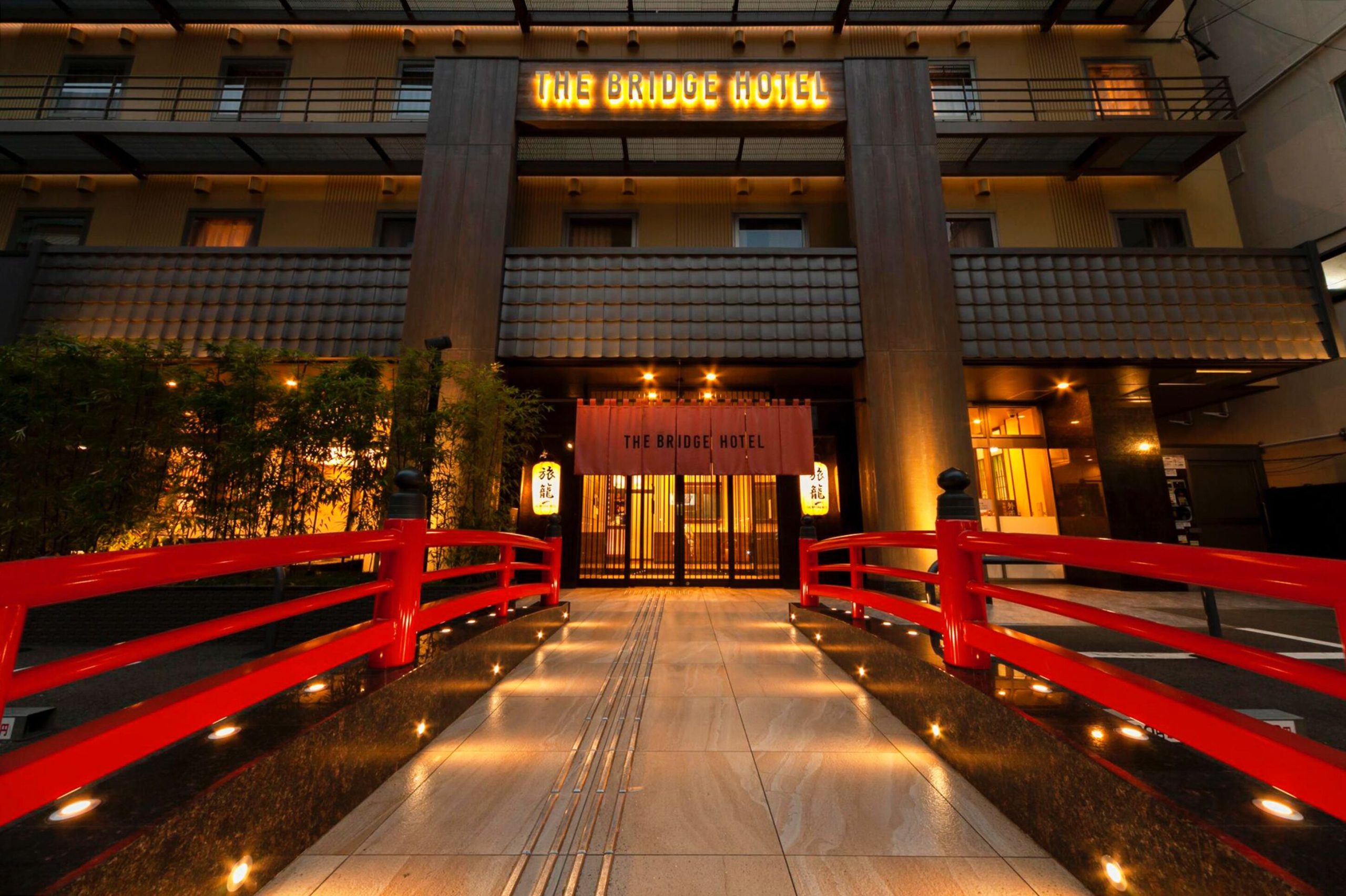 A red bridge surrounds The Bridge Hotel, a top accommodation in Shinsaibashi, Osaka. The hotel entrance has two signs reading "The Bridge Hotel".