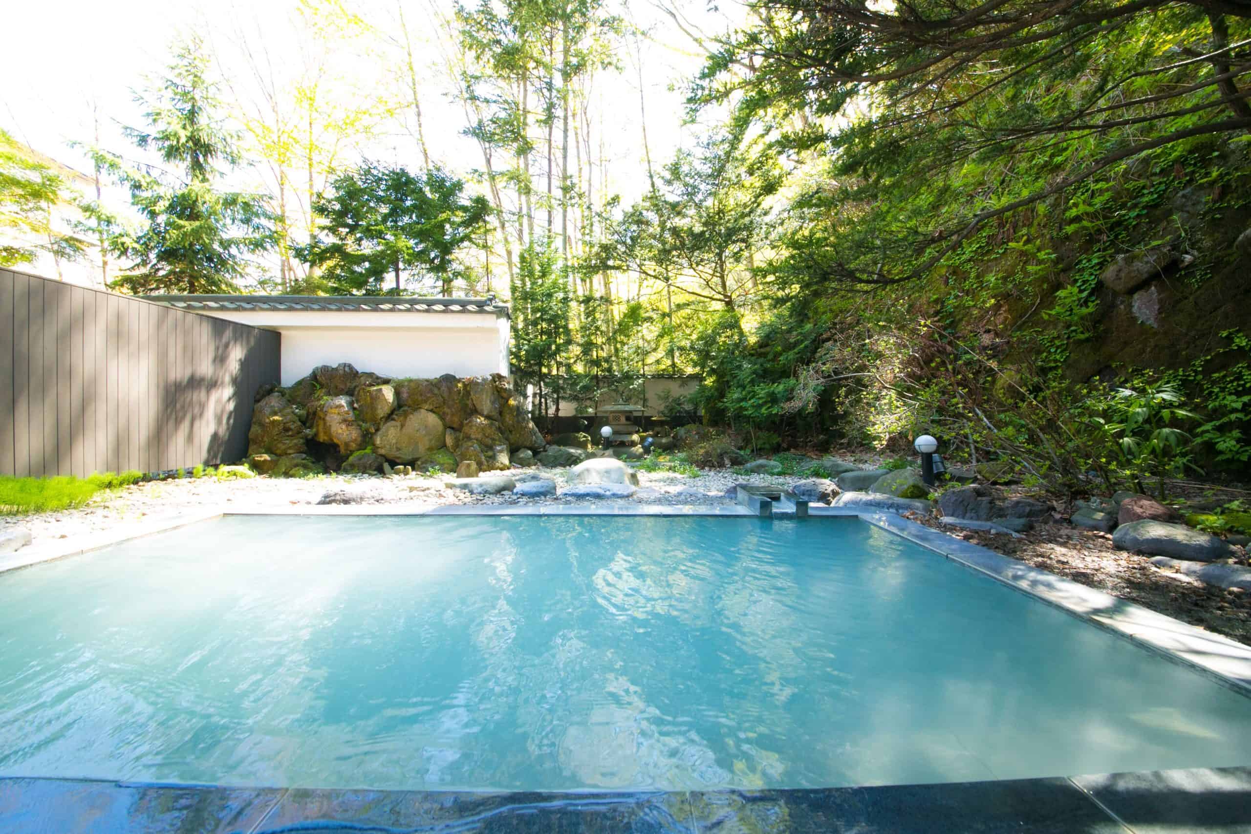 Open-air hot spring surrounded by trees and natural rock at Bourou Noguchi Noboribetsu, one of the most exclusive 5 star hotels near Sapporo.
