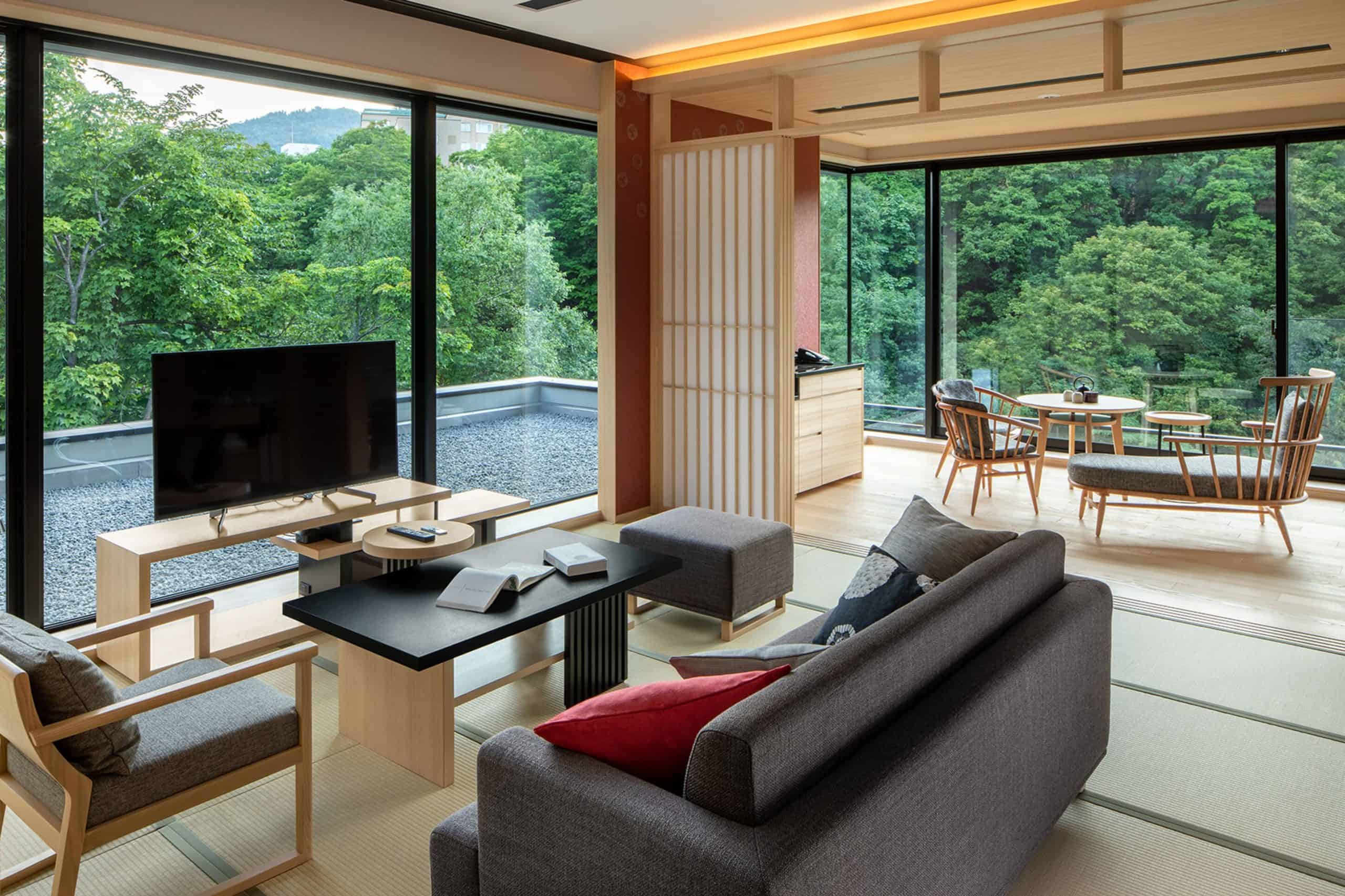 Spacious tatami living room at Chalet Ivy Jozankei featuring modern Japanese design, a cozy seating area, and panoramic forest views through floor-to-ceiling windows.