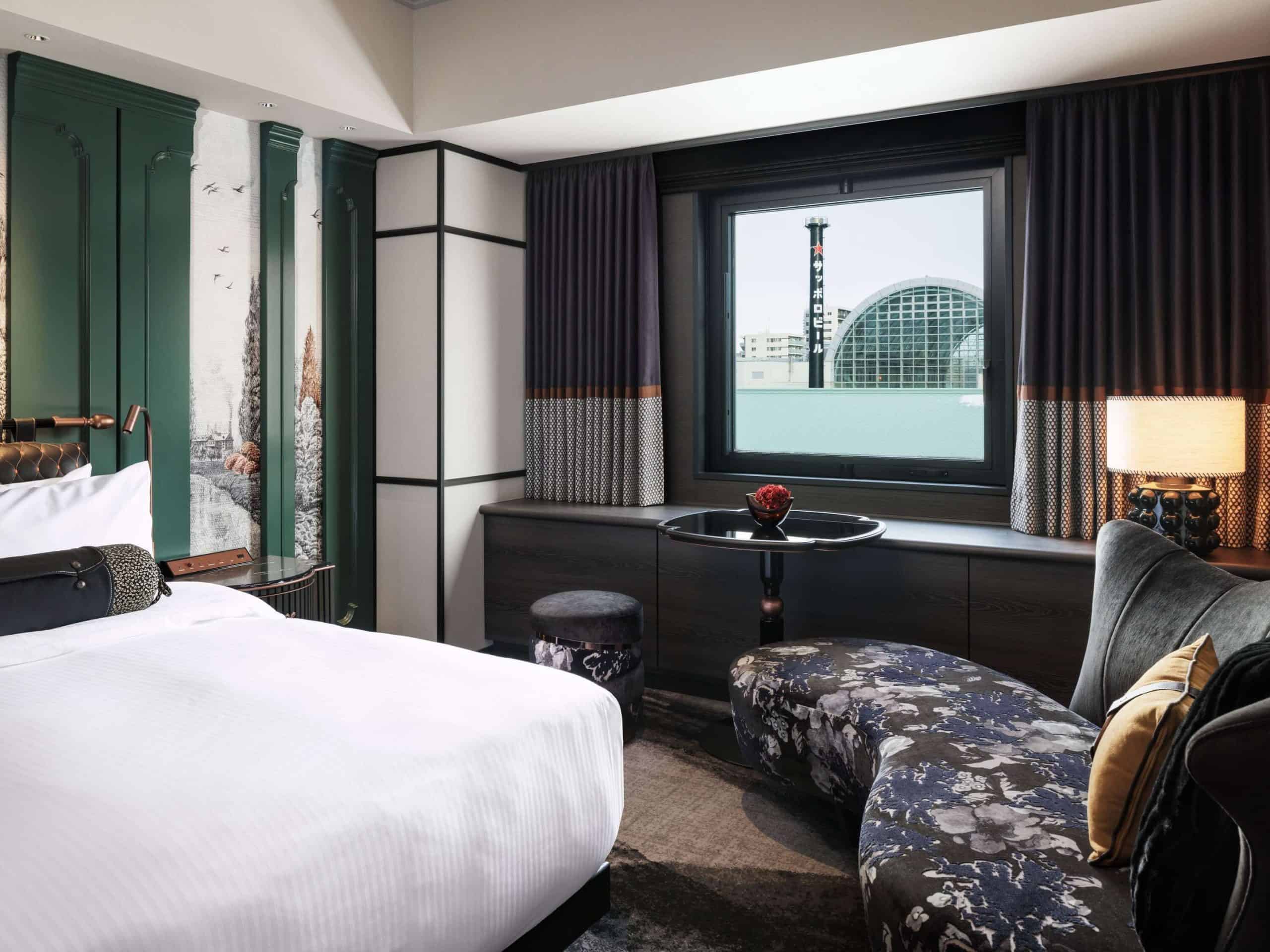 A luxurious guest room at Hotel Sosei Sapporo – MGallery Collection, featuring plush bedding, artistic paneling, and a city view framed by soft drapes.