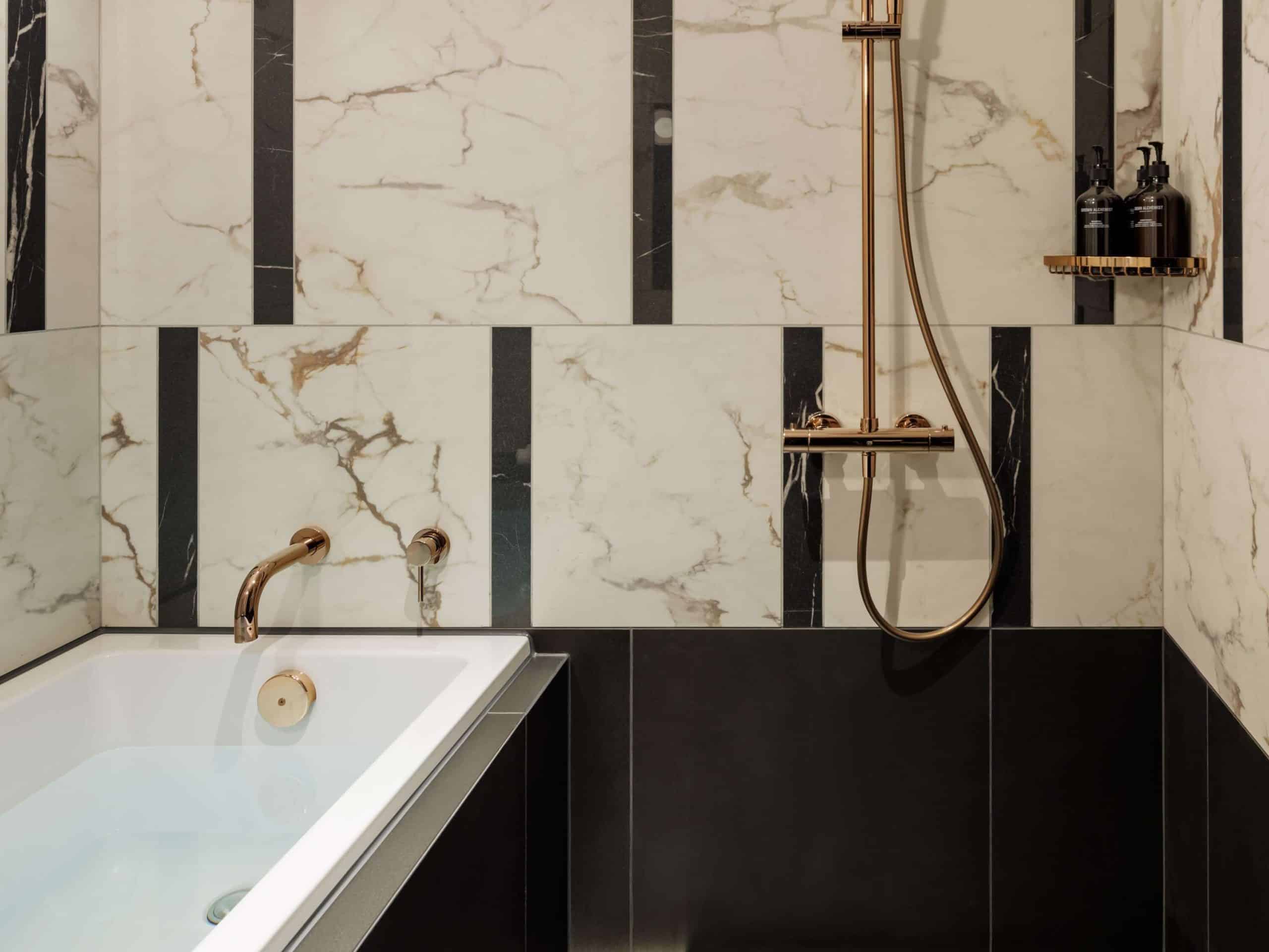 A sleek marble-tiled bathroom at Hotel Sosei Sapporo – MGallery Collection, complete with a deep soaking tub and gold-accented rain shower.