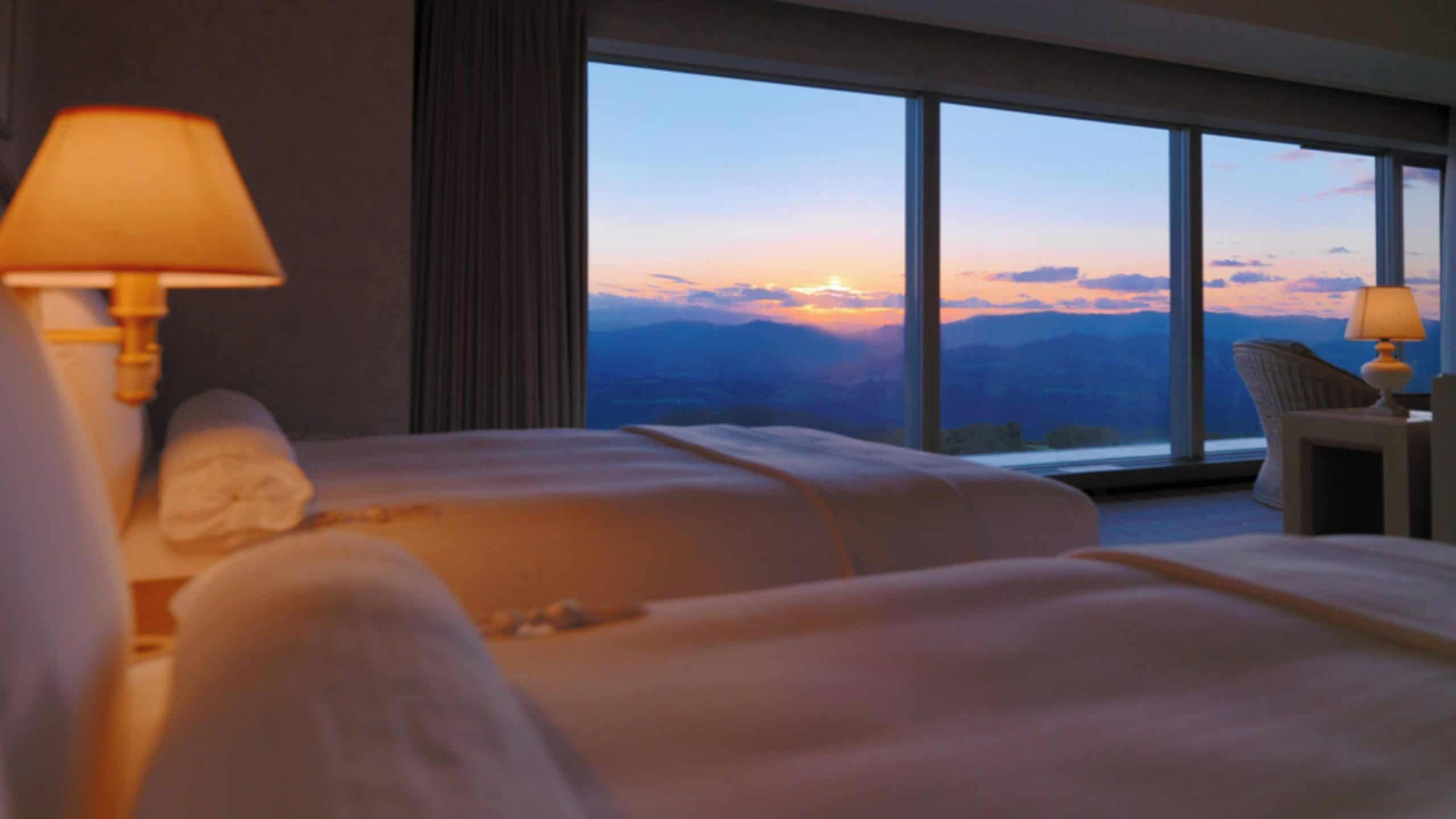 Cozy twin room at The Windsor Hotel Toya with floor-to-ceiling windows showcasing a glowing mountain sunset—ideal for travelers seeking refined stays near 5 star hotels in Sapporo.