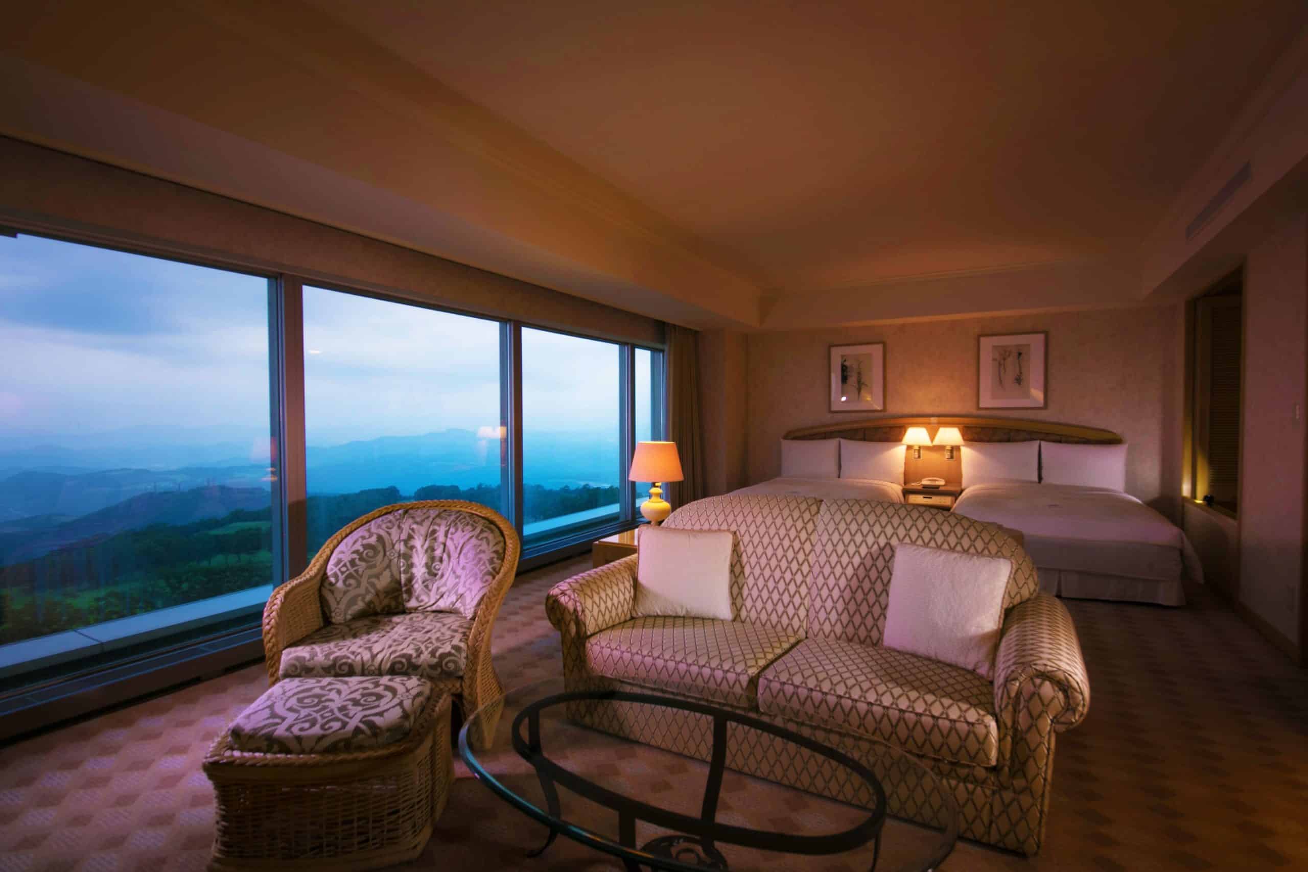Warm and inviting suite at The Windsor Hotel Toya featuring plush seating and expansive windows with forested mountain views, showcasing the classic charm of this luxury 5 star hotel near Sapporo.