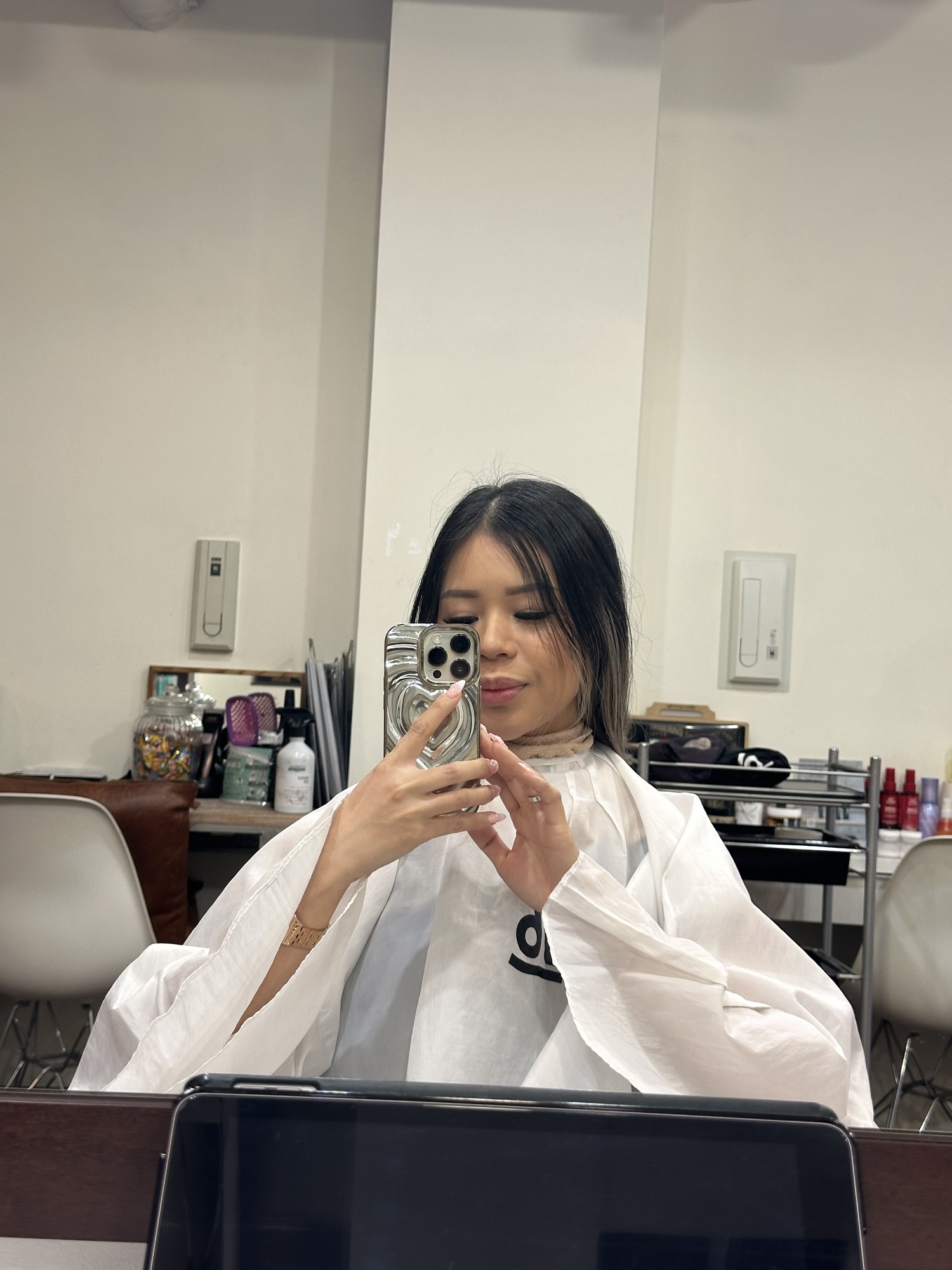 A girl with black hair and a white clothing cover sitting in Number76 salon, an English speaking hair salon in Tokyo, Japan.