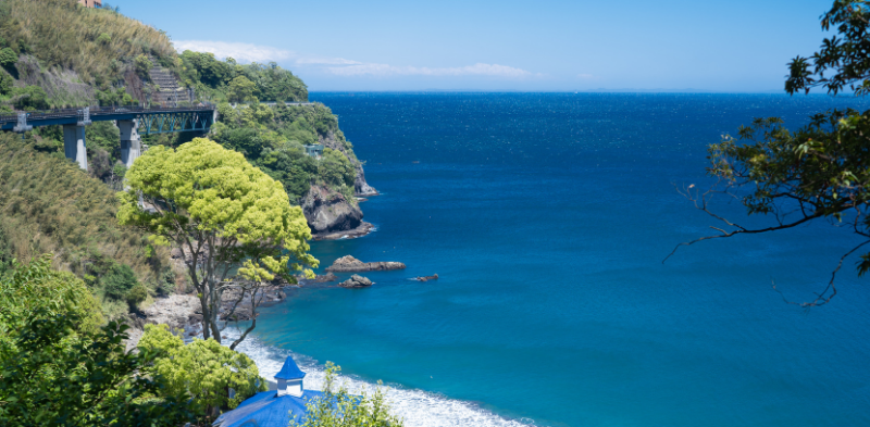 Scenic coastal view of Nishikigaura in Atami with turquoise blue water, steep cliffs, and lush green trees along the coastline.