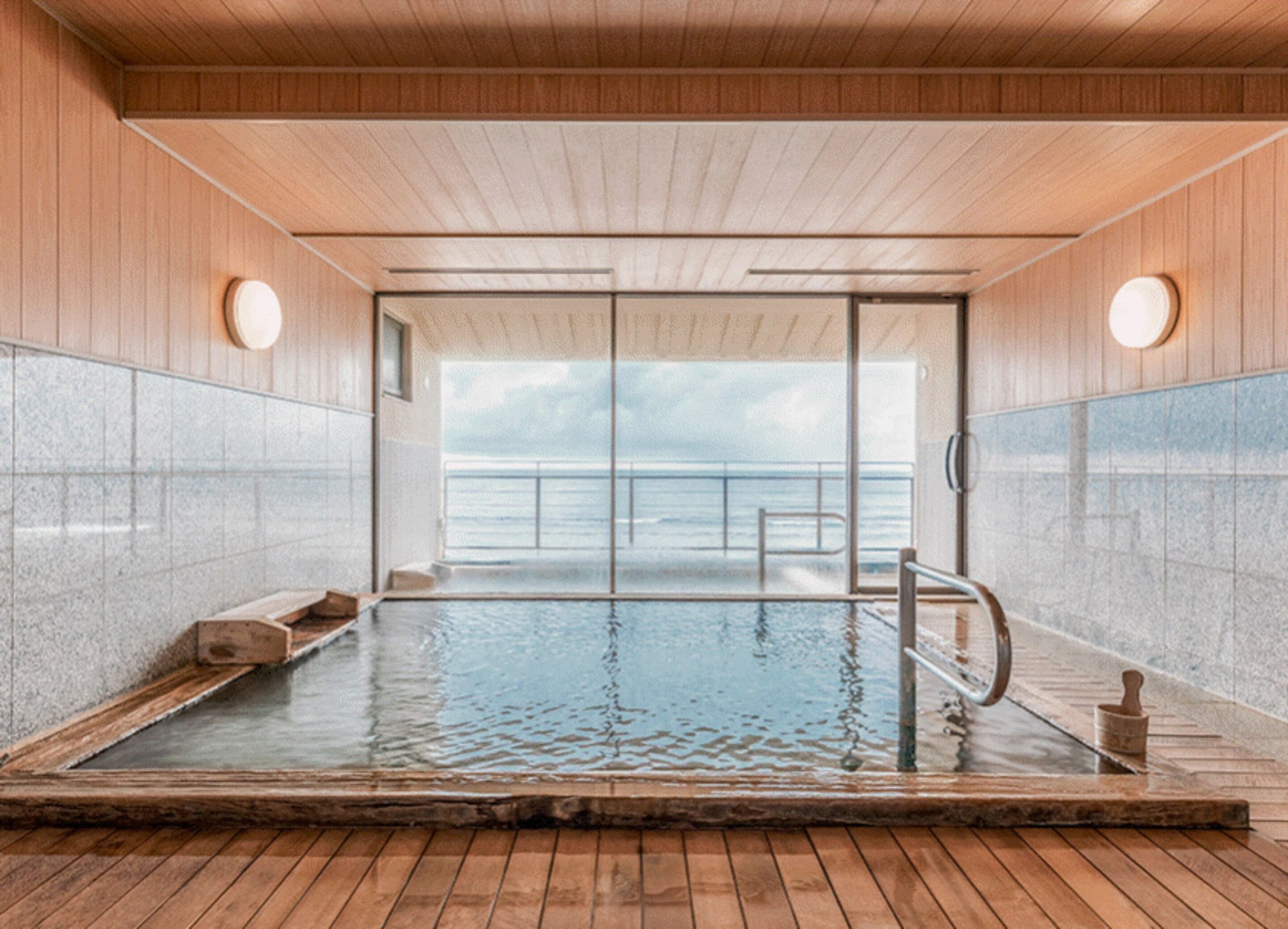 Serene indoor onsen bath at Wakamatsu Hot Spring Resort overlooking the sea through large glass windows