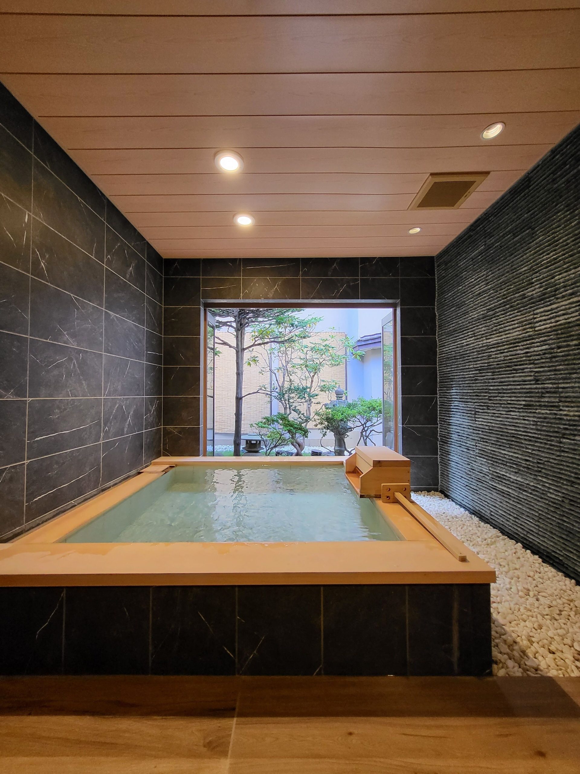 Modern indoor onsen with sleek black tiles and a view of a peaceful garden courtyard at Wakamatsu Hot Spring Resort