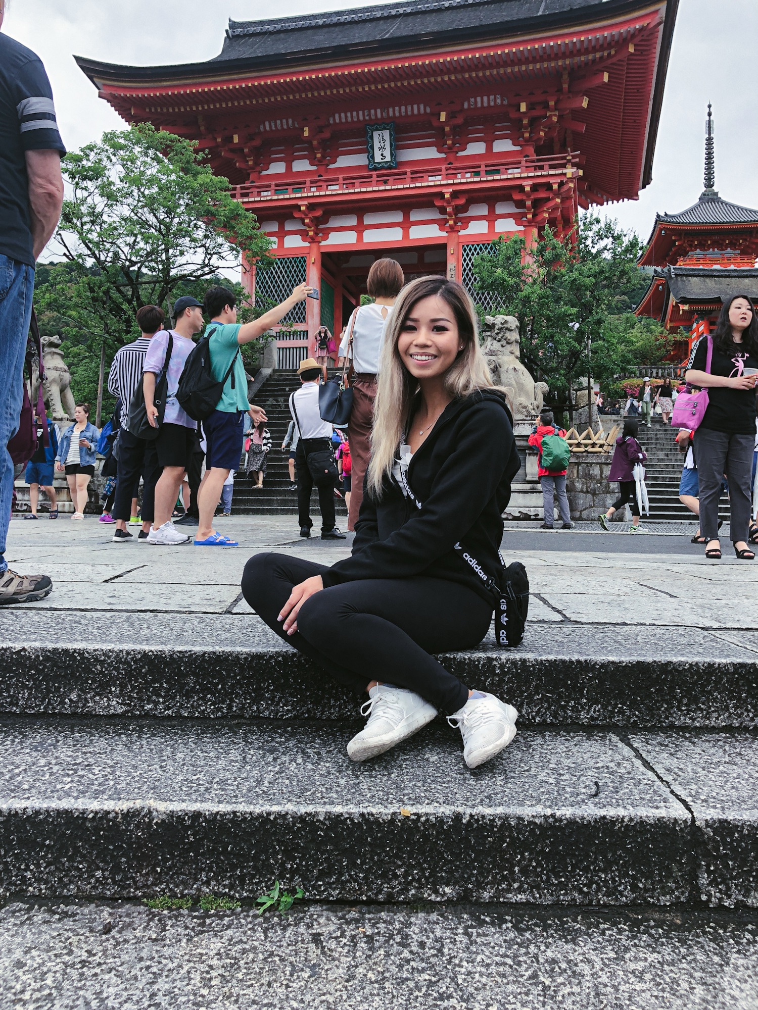A smiling woman sits on the stone steps in front of Kiyomizu-dera’s iconic bright red gate, a must-see stop on any 1 day Kyoto itinerary.