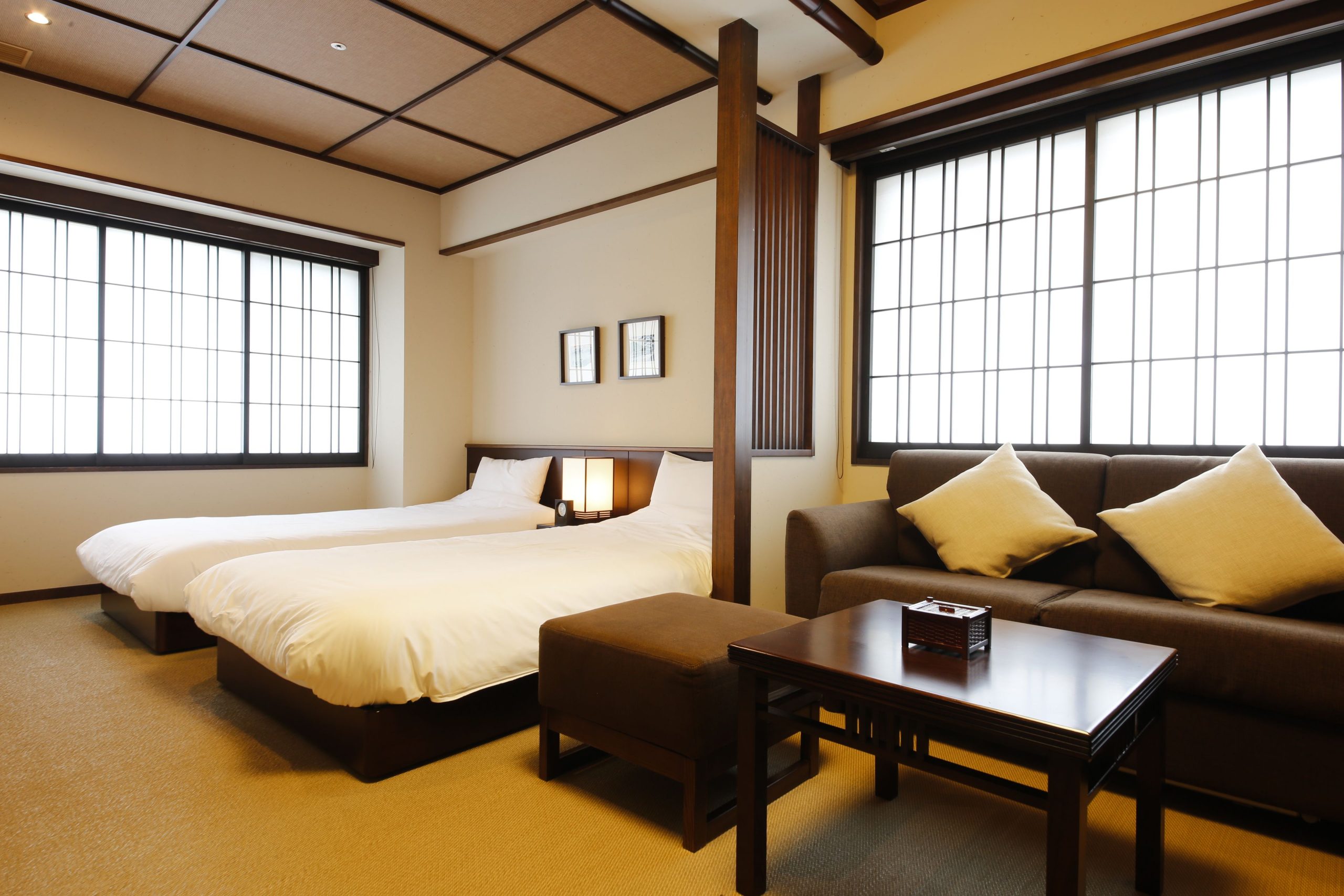 Modern Japanese-style guest room at Arashiyama Kadensho Ryokan, featuring twin beds, a sofa, and shoji-style windows.