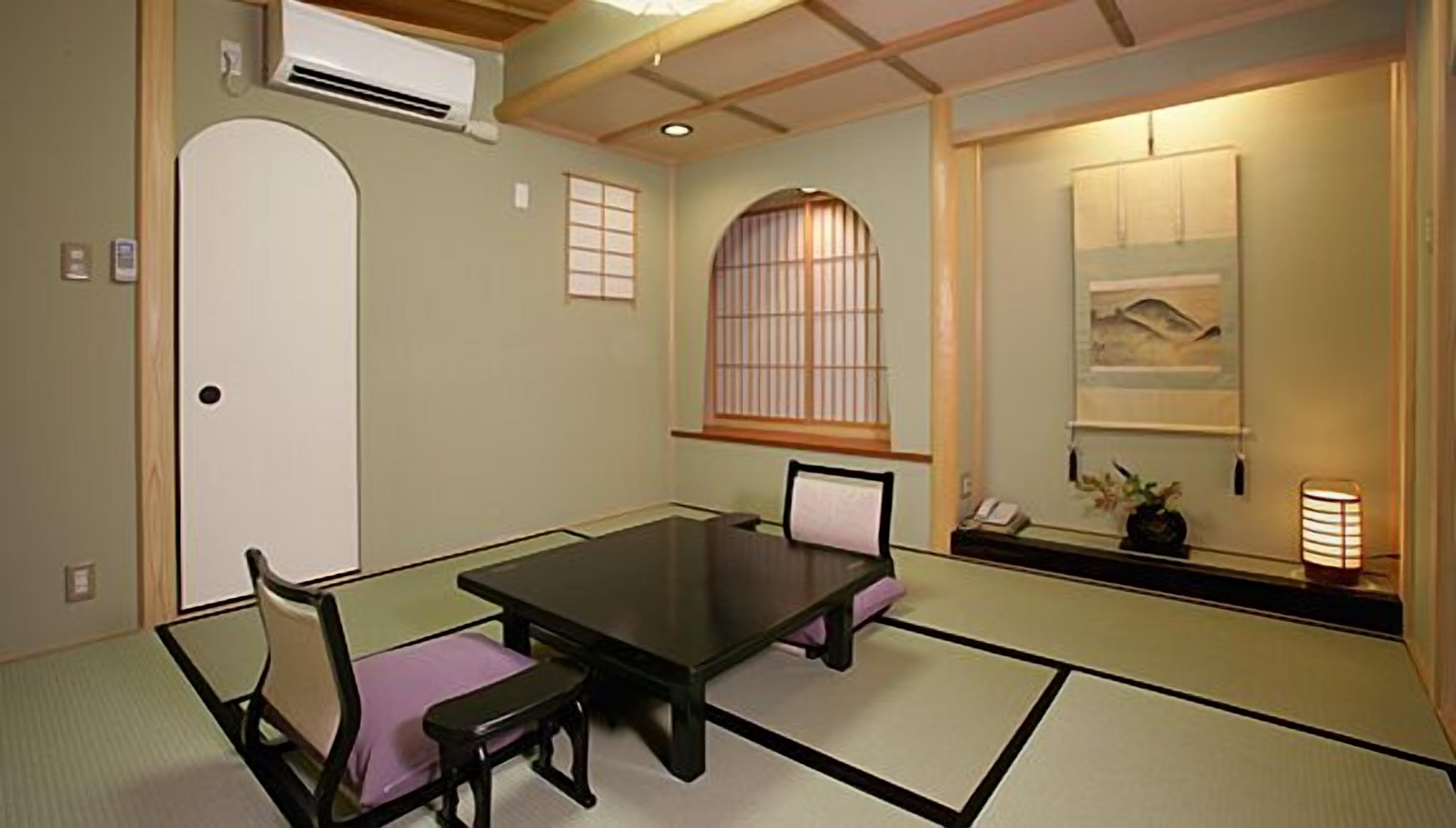 Minimalist tatami room at Hanaikada Ryokan, with a low table, floor chairs, and a hanging scroll for a classic Japanese atmosphere.