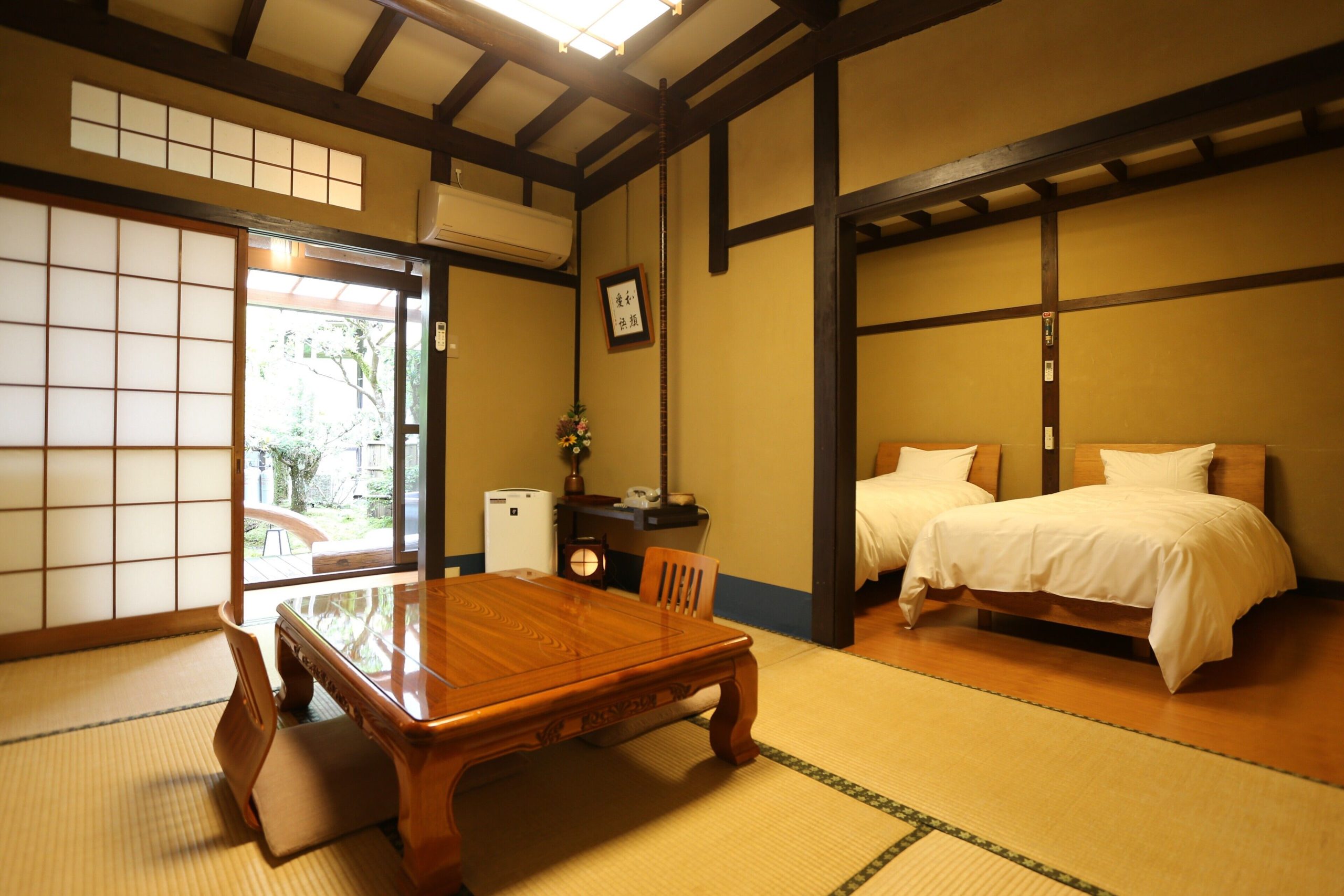 Spacious tatami room at Momijiya Bekkan Kawanoiori, blending traditional Japanese design with Western-style twin beds and garden access.