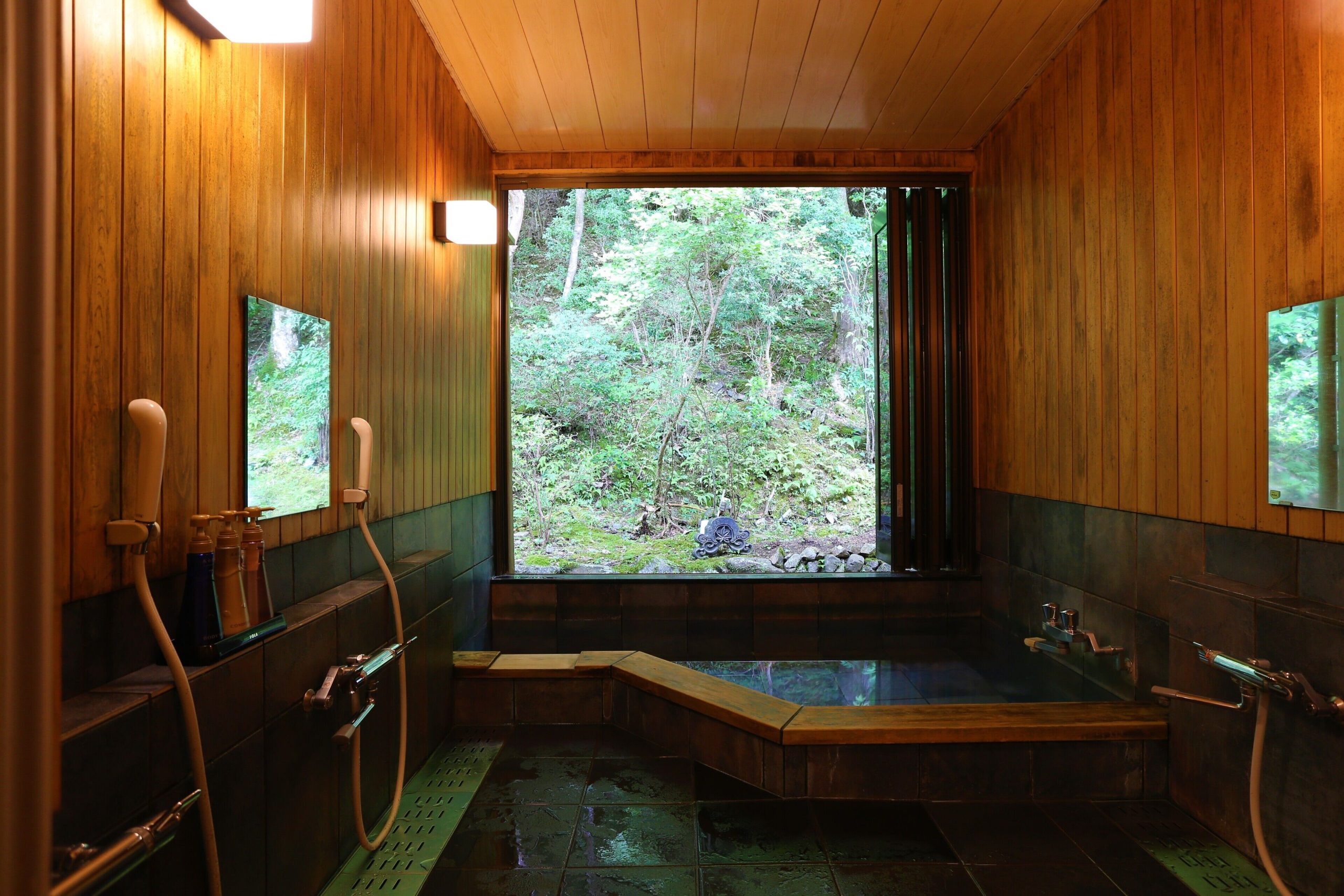 Oval open-air bath with bamboo fencing and lantern lighting at Momijiya Bekkan Kawanoiori, creating a serene evening bathing experience.