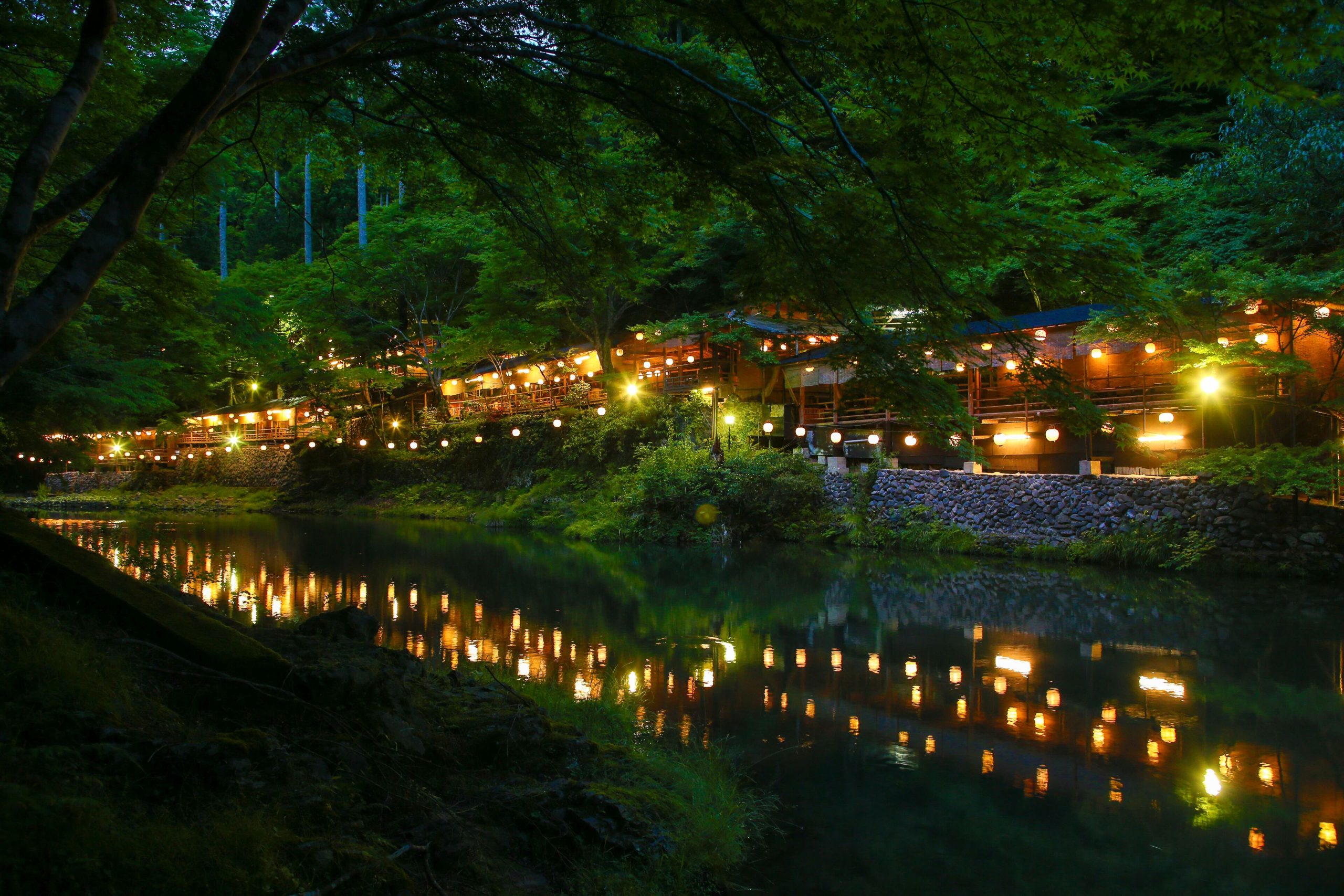 Riverside view of Momijiya Bekkan Kawanoiori, beautifully illuminated at night with glowing lanterns reflecting on the water.
