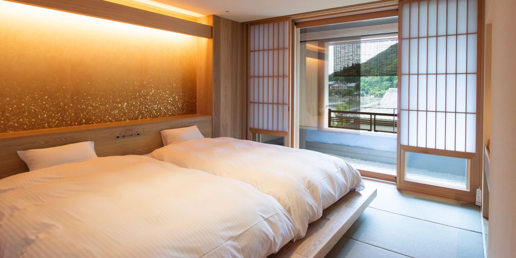 A modern Japanese-style twin room at Ryotei Rangetsu, with soft lighting, shoji doors, and mountain views — perfect for a stay at an Arashiyama ryokan.