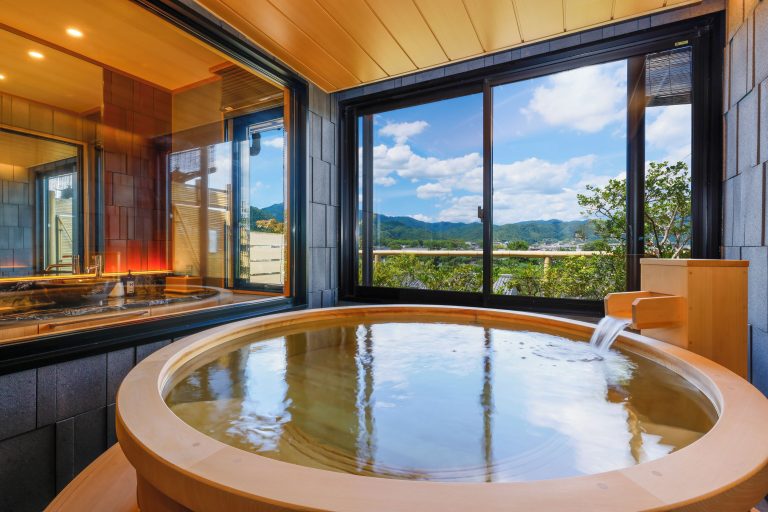 Indoor wooden bath at Togetsutei Ryokan, with a large open window facing the forest and modern shower stations for pre-bathing.