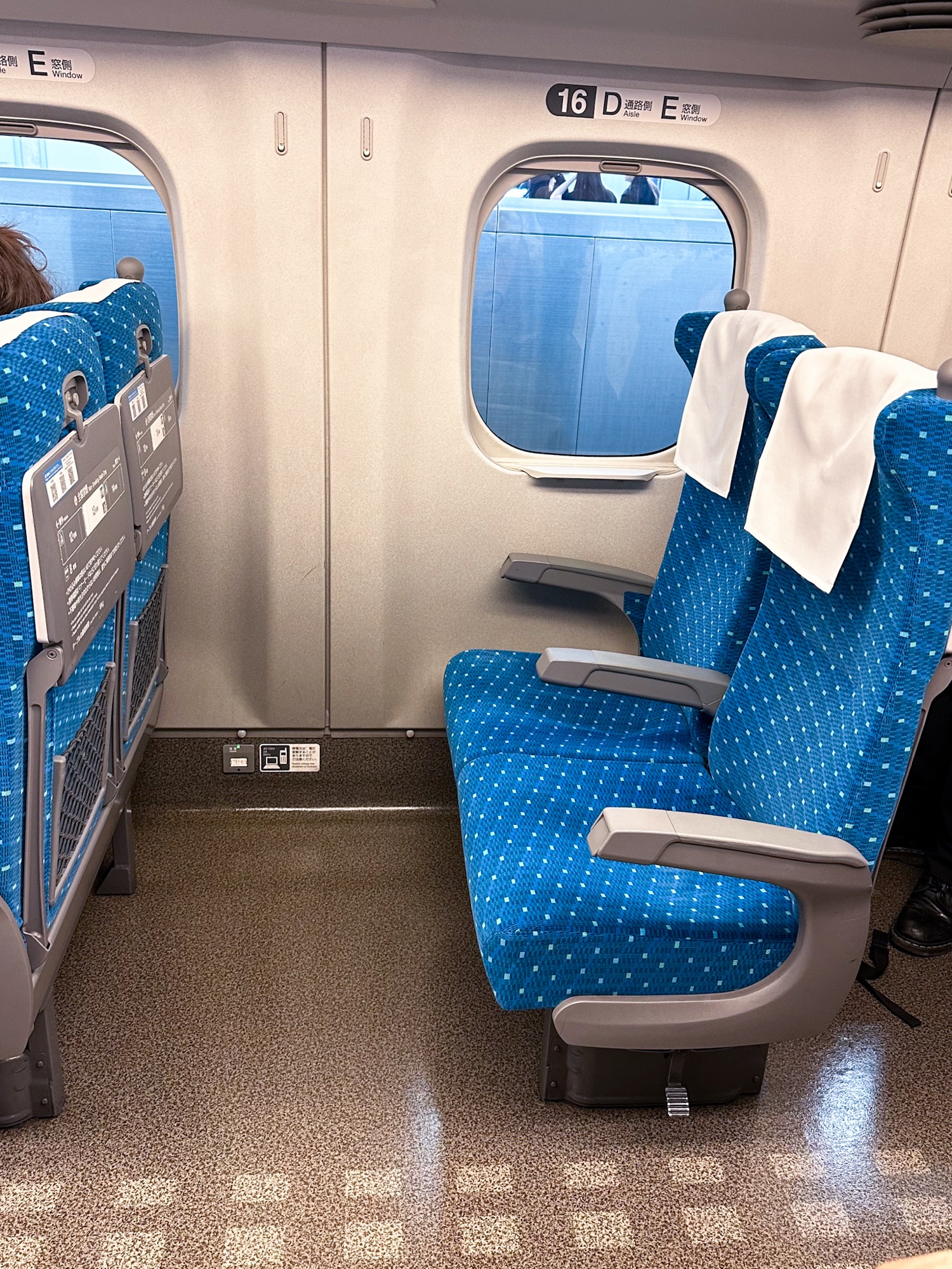 A view inside the Shinkansen, where limited storage between the seat and overhead highlight the benefit of using Japan’s luggage delivery service.