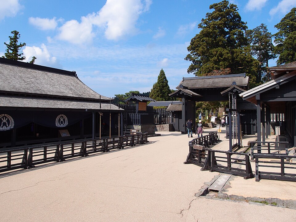 The restored Edo-period Hakone Checkpoint with traditional wooden gates and black-roofed buildings, set against tall cedar trees and a bright blue sky in Hakone, Japan.