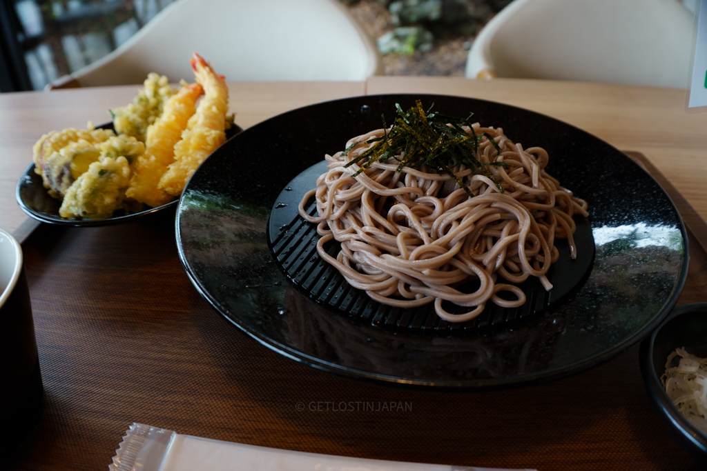 Cold soba noodles served on a black plate topped with shredded seaweed, accompanied by a side of assorted tempura including shrimp and vegetables at Hatsuhana Soba in Hakone, Japan.