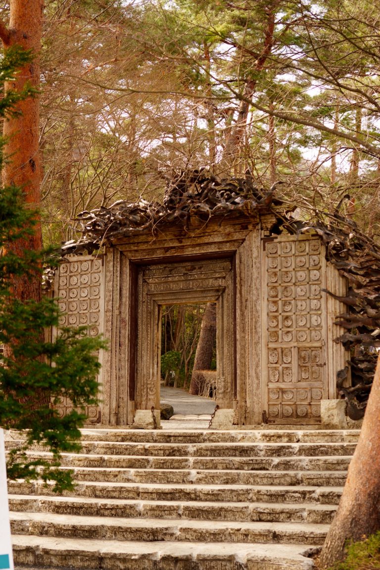 The wooden, intricately carved entrance gate of the Itchiku Kubota Art Museum surrounded by trees.