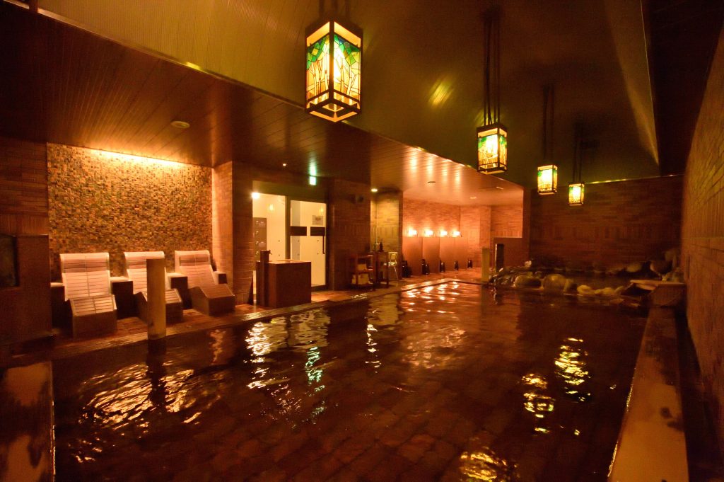 Relaxing indoor onsen at Dormy Inn Otaru, featuring soft amber lighting and stone accents — a great Otaru onsen hotel for unwinding after sightseeing.