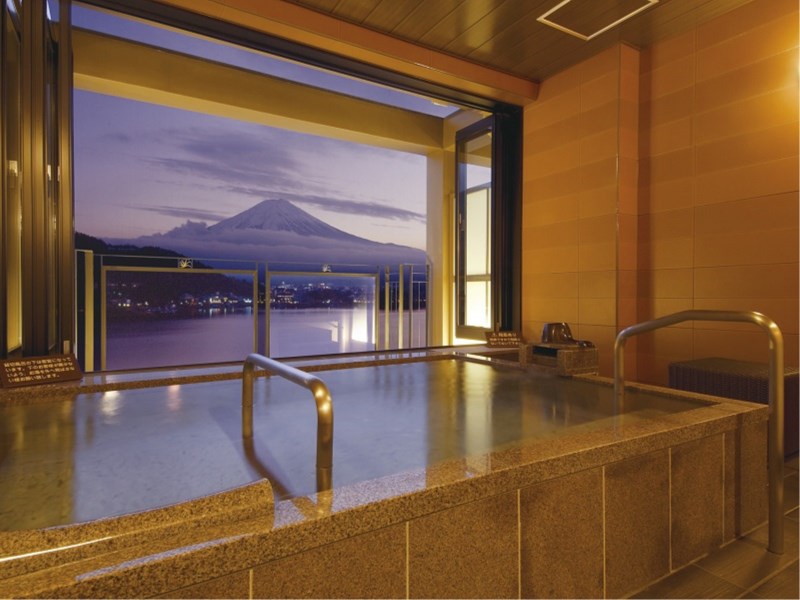 A private onsen overlooking Lake Kawaguchiko and Mount Fuji during dusk through large evening windows.